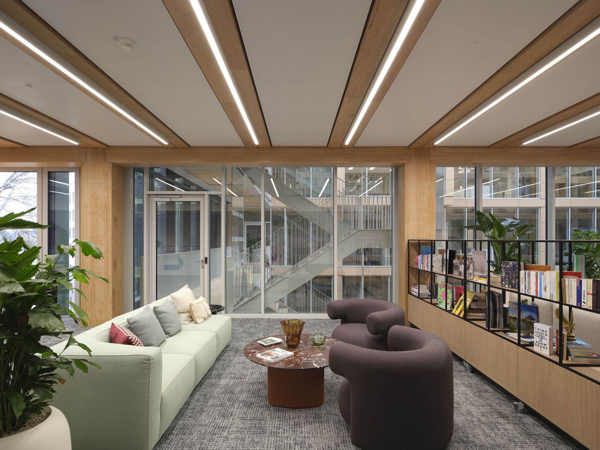 Seating area with timber-framed glazing overlooking a central staircase within the atrium