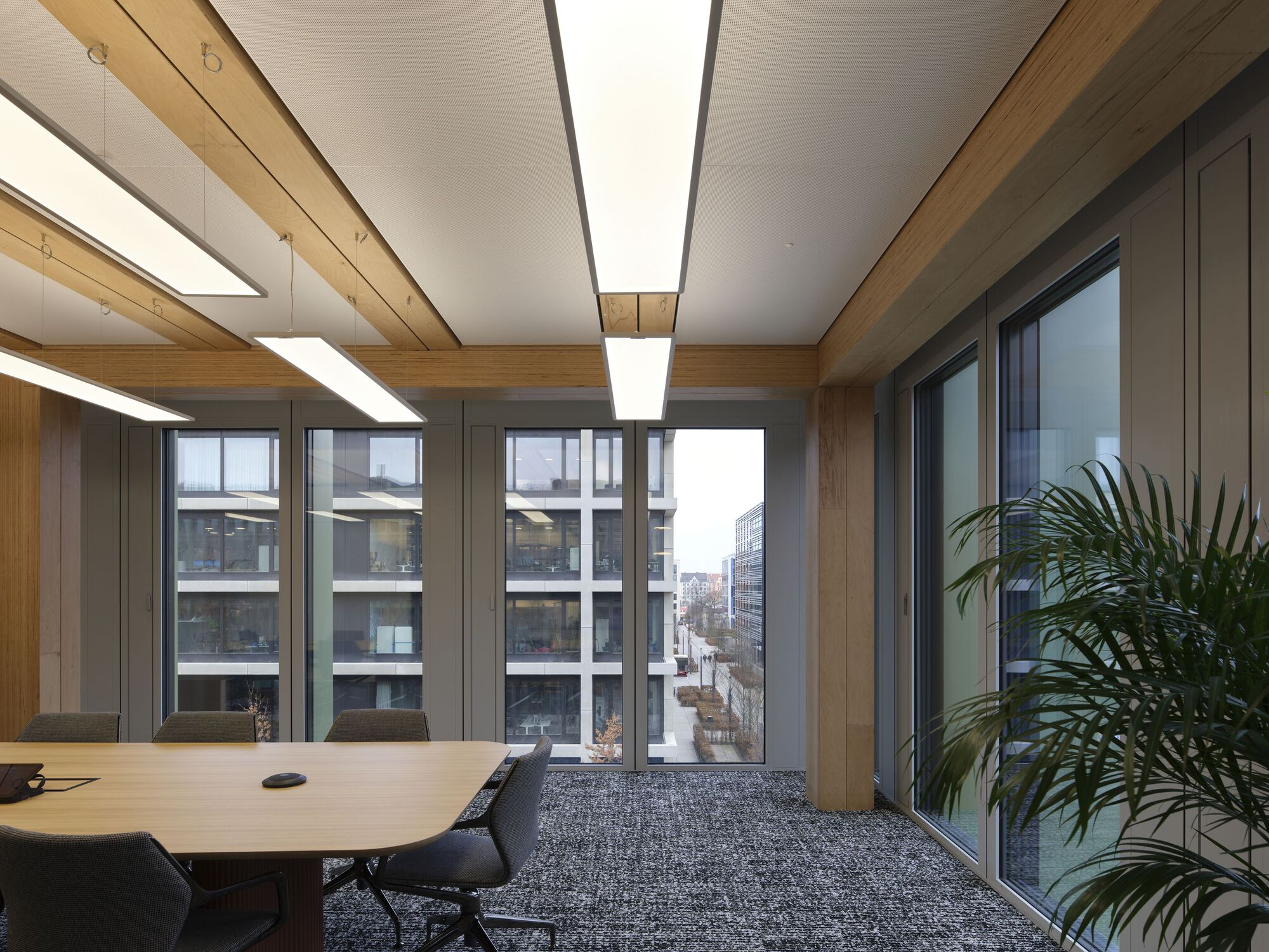 Meeting room with corner glazing and timber beam ceiling framing views of neighboring buildings
