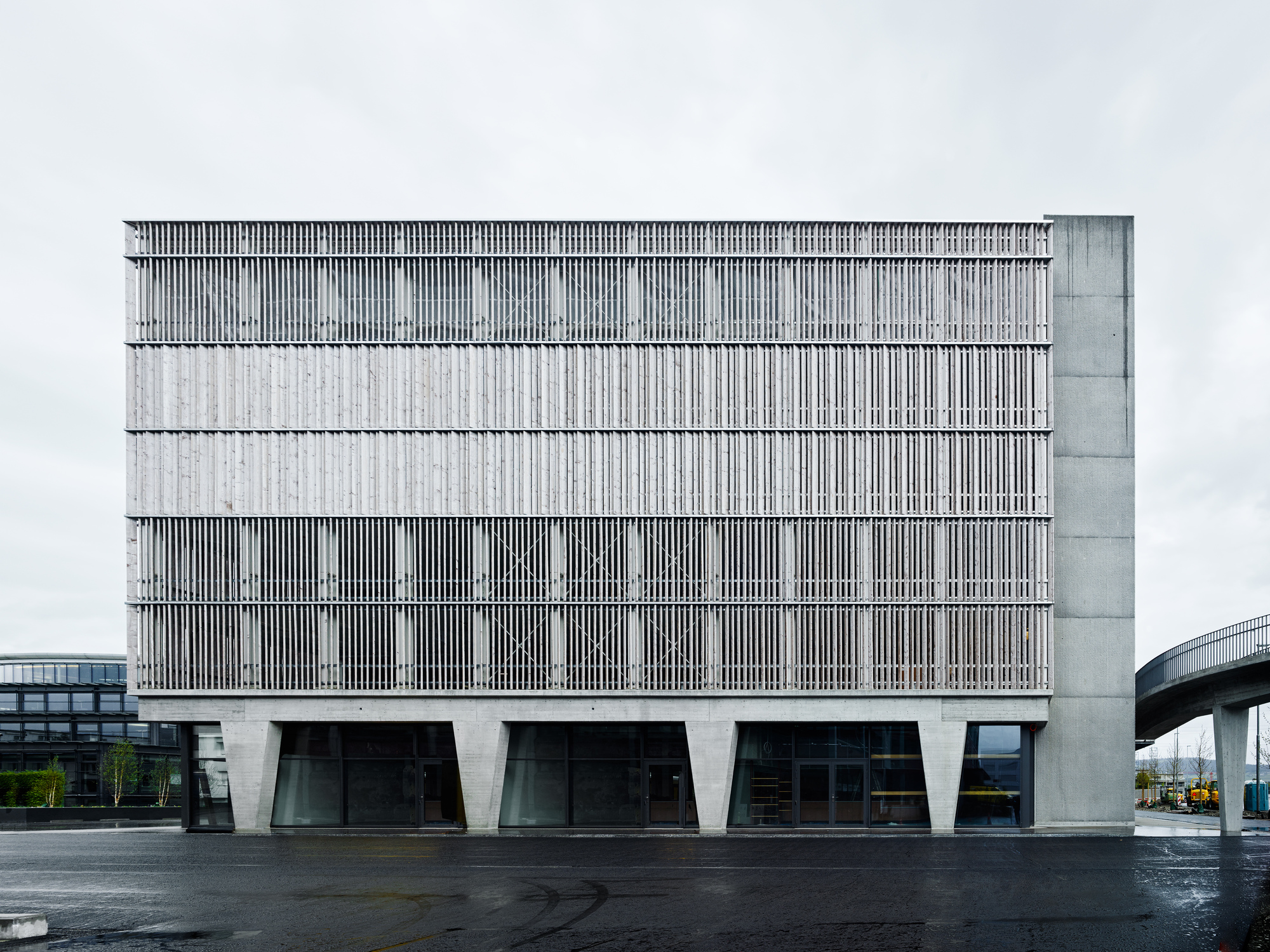 Frontal view of the louvered facade with alternating bands above angled ground floor columns after rainfall