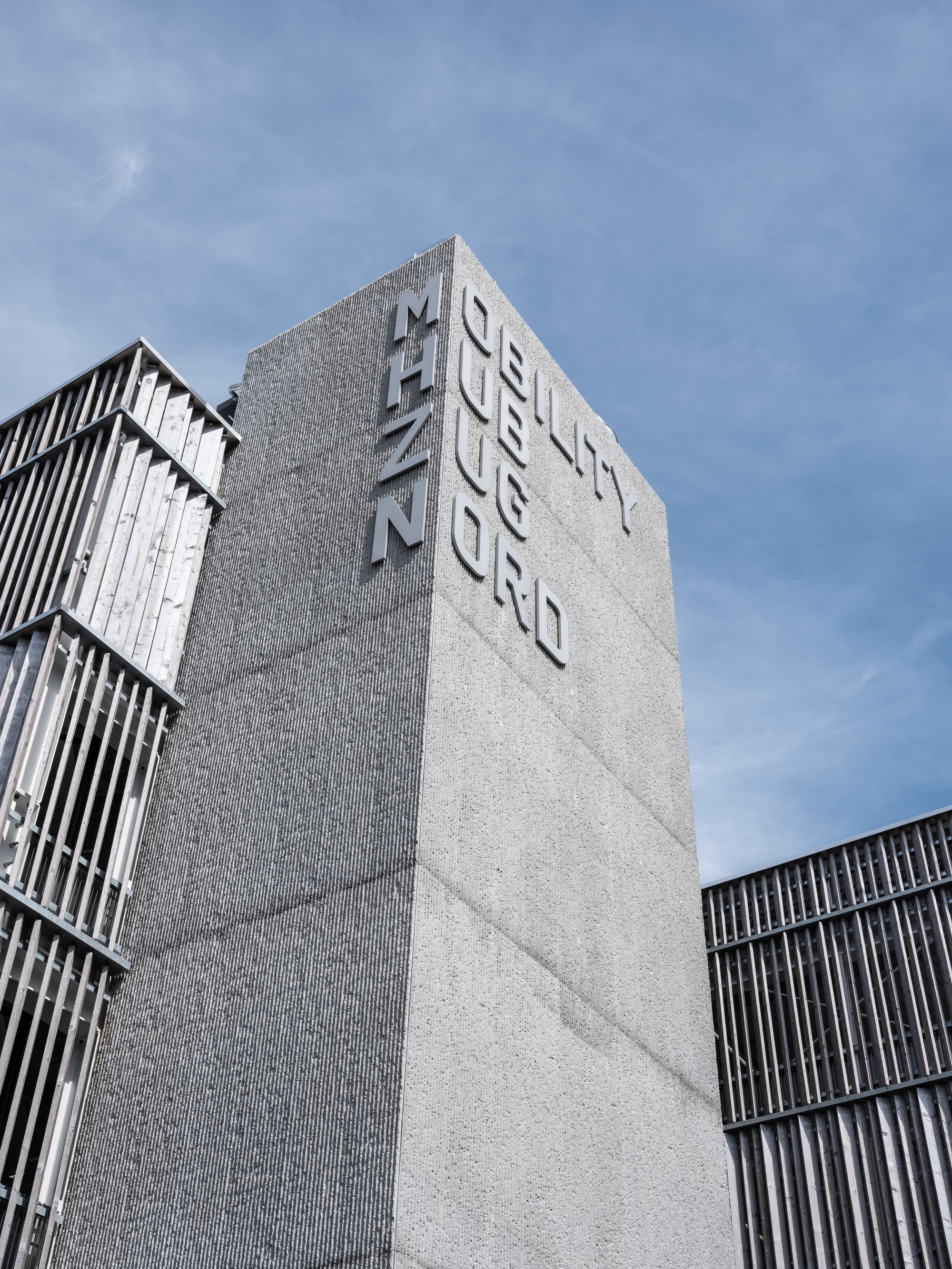 Upward view of the textured concrete tower with raised letterforms against a blue sky