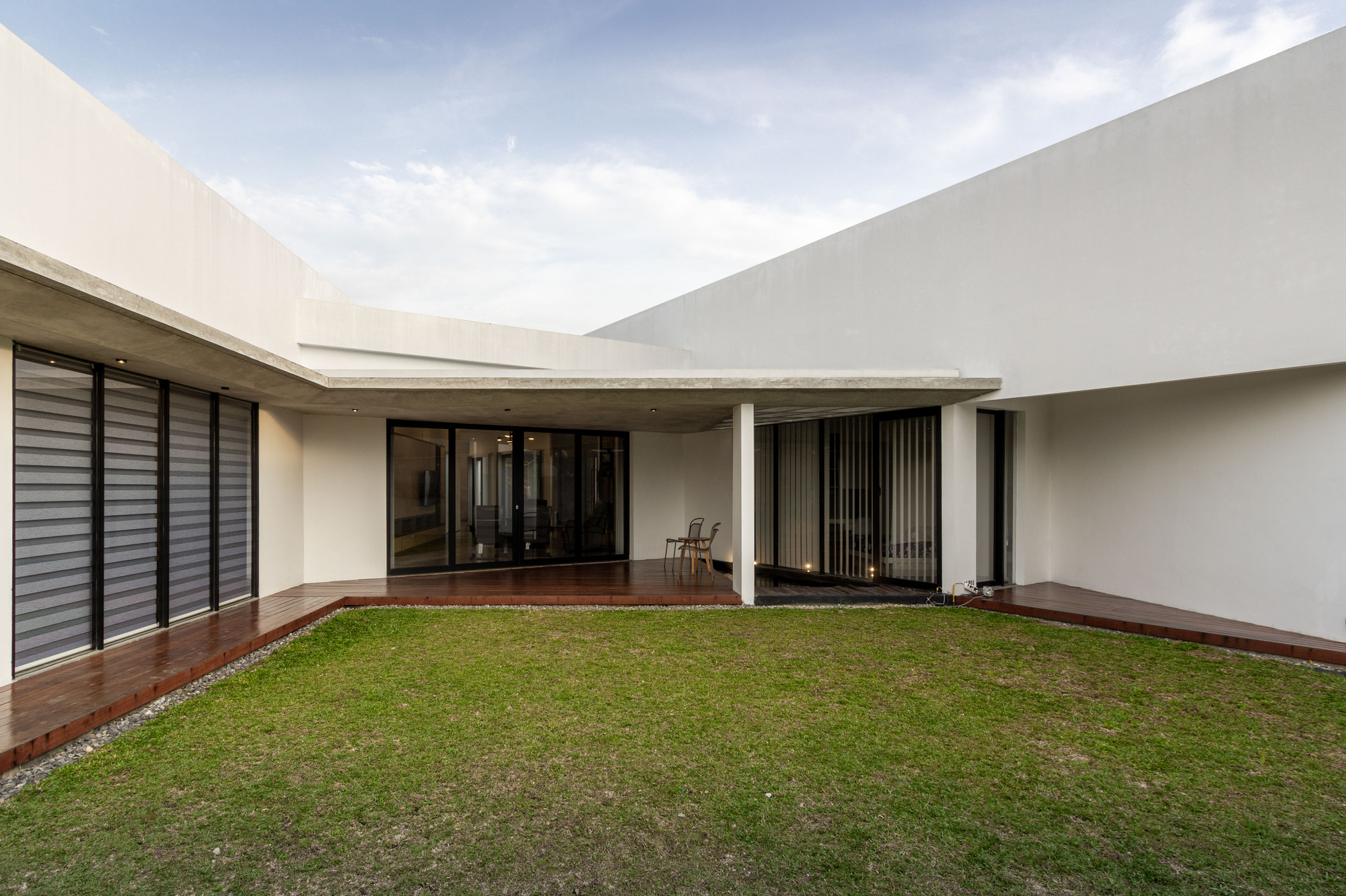 Private courtyard with grass lawn bordered by timber deck and white rendered walls under cloudy sky