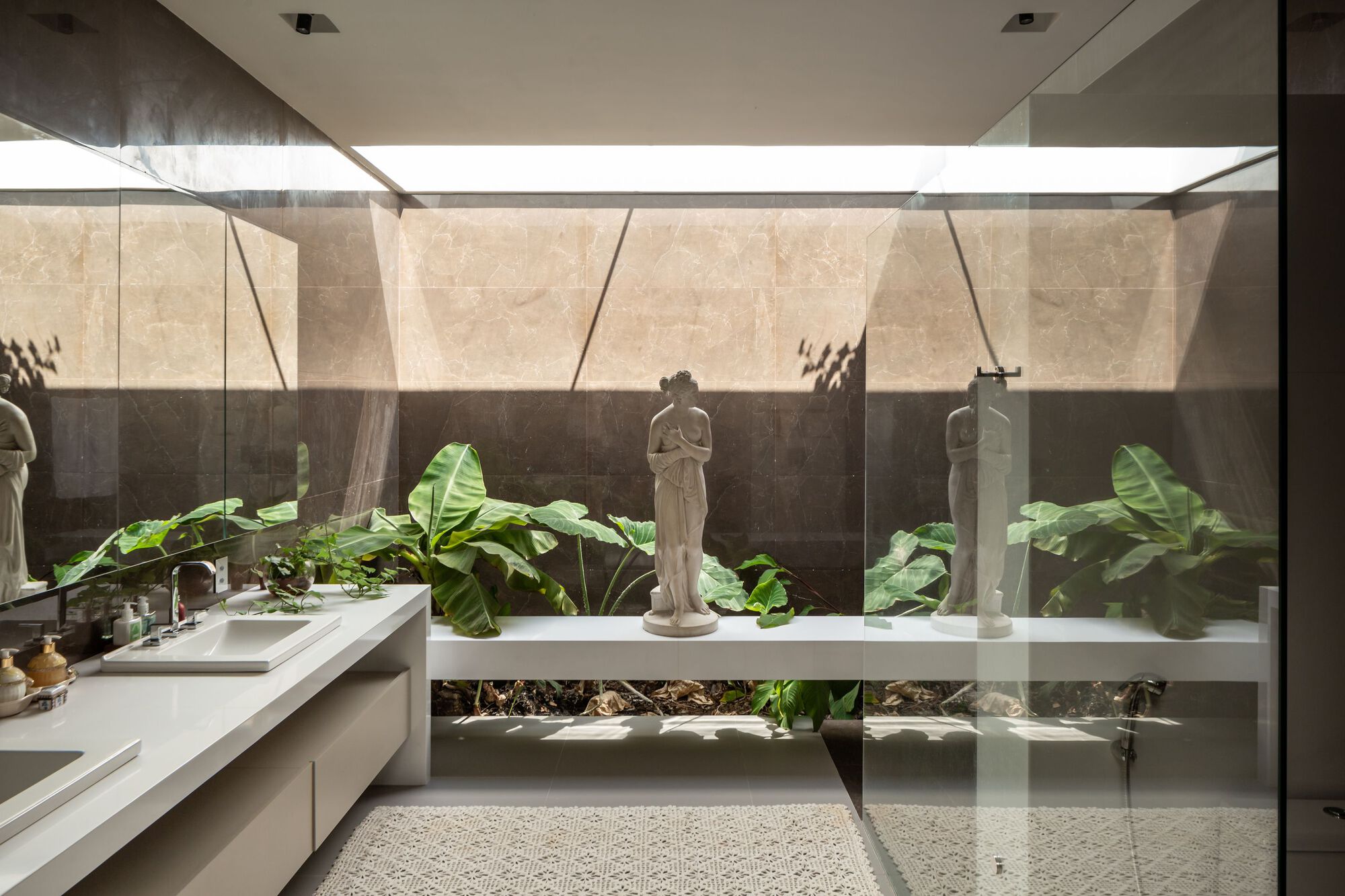 Bathroom with stone-clad wall, integrated planter bed of tropical foliage, and sculpture behind glass partition