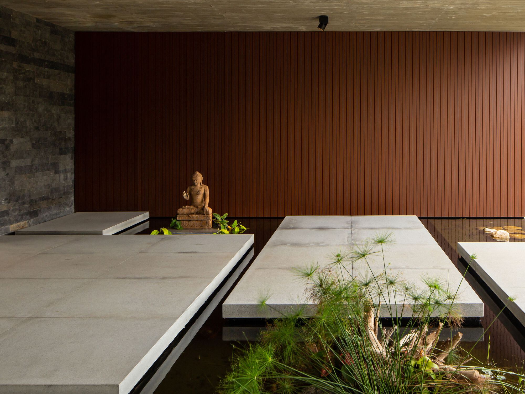 Interior courtyard with concrete platform over reflecting pool, vertical wood wall and stone Buddha sculpture