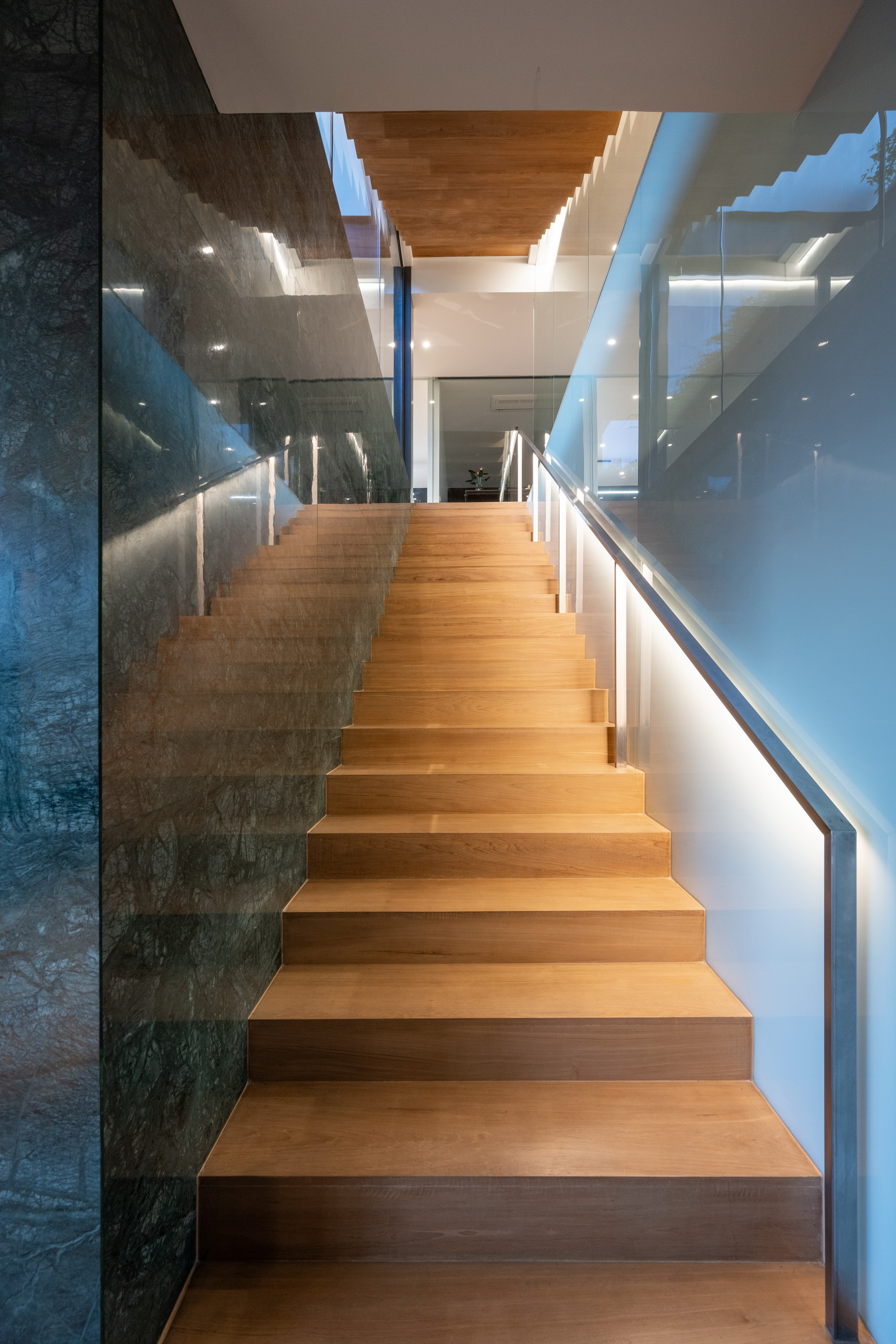 Timber staircase with integrated handrail lighting ascending between white walls and textured stone cladding panels