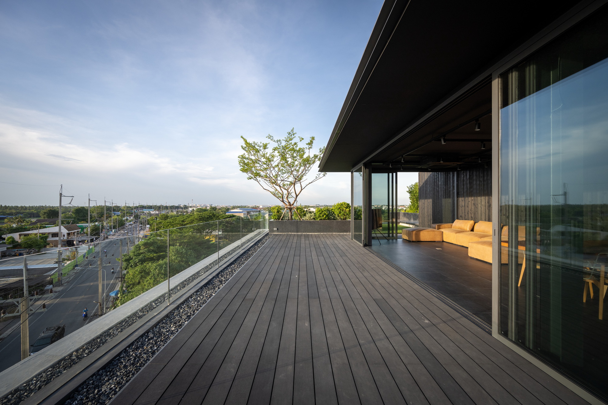 Timber deck terrace with planted tree and deep roof overhang overlooking distant streetscape at evening
