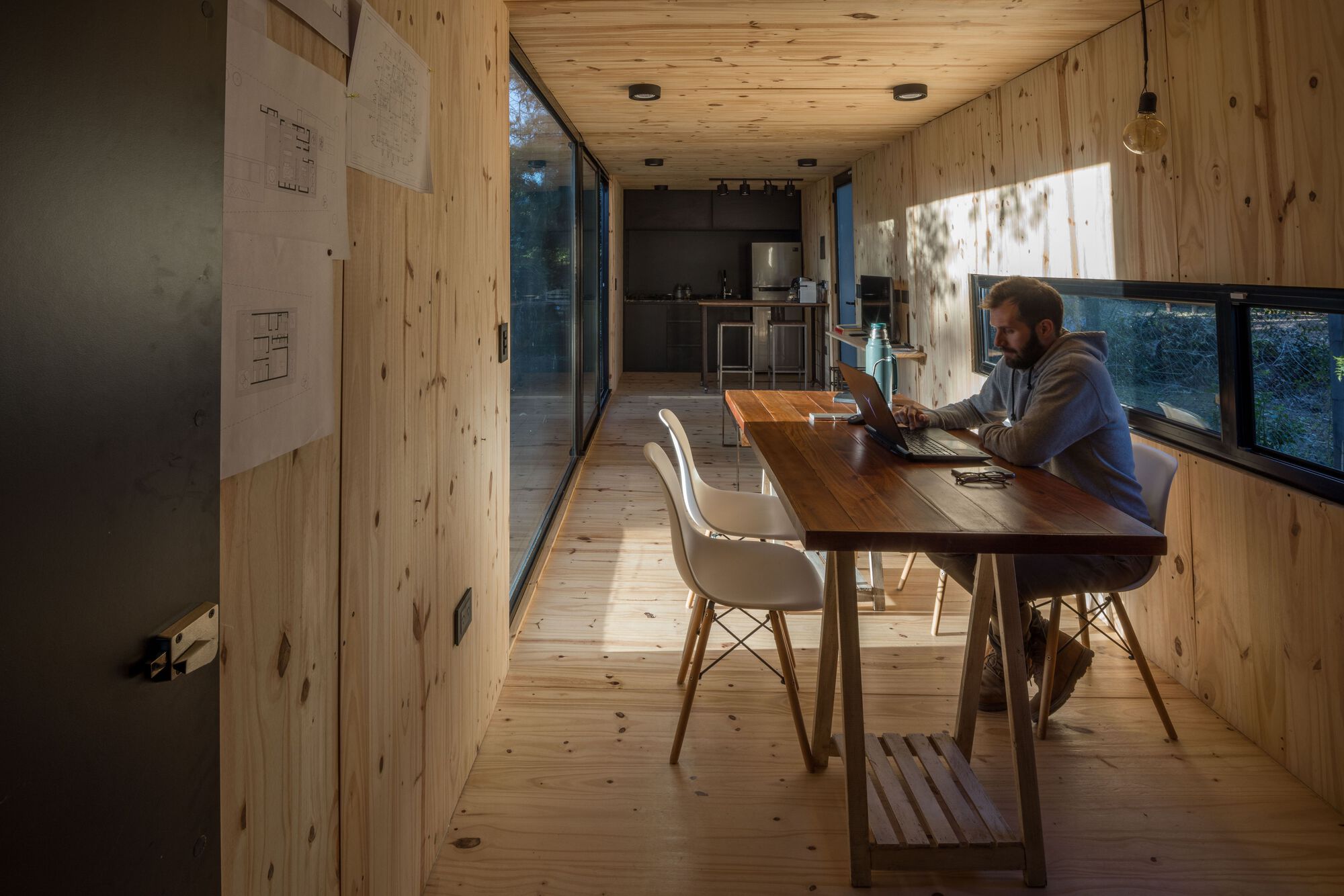 Person working at a timber table in the pine-lined interior with ribbon windows on both sides
