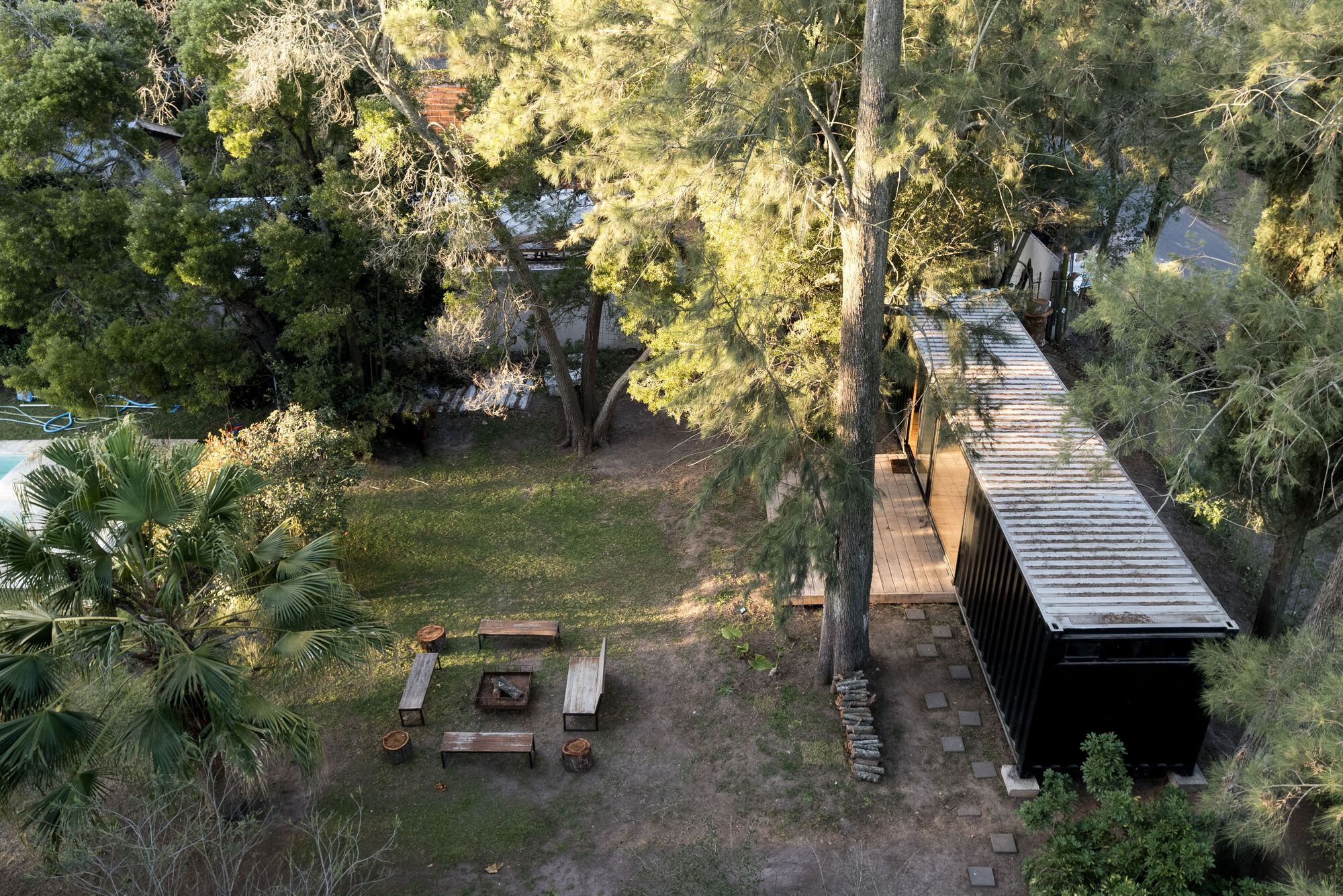 Aerial view of a corrugated metal pavilion and outdoor fire pit surrounded by mature trees