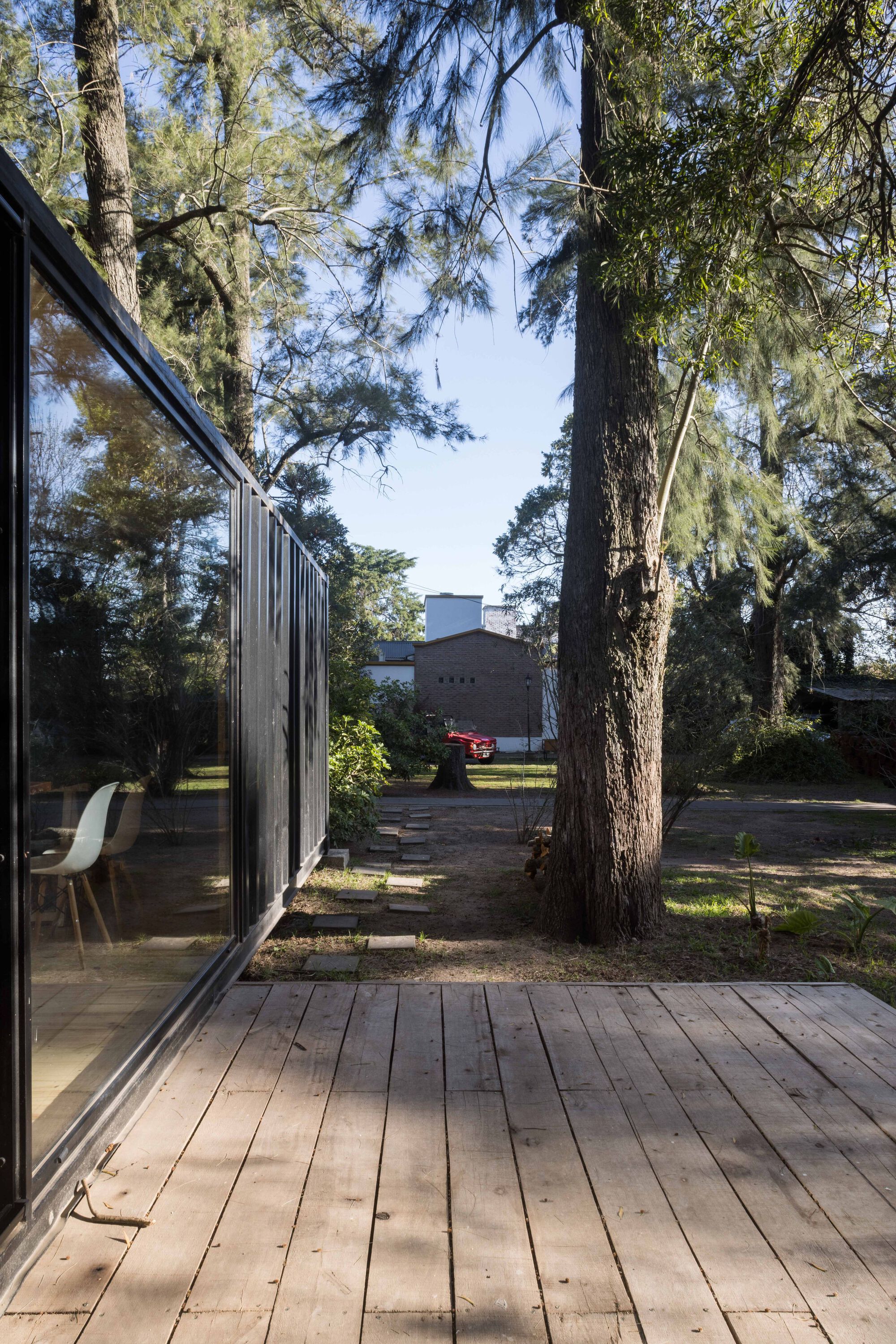 Timber deck extending from sliding glass doors with vertical black metal cladding and pine trunks framing the view