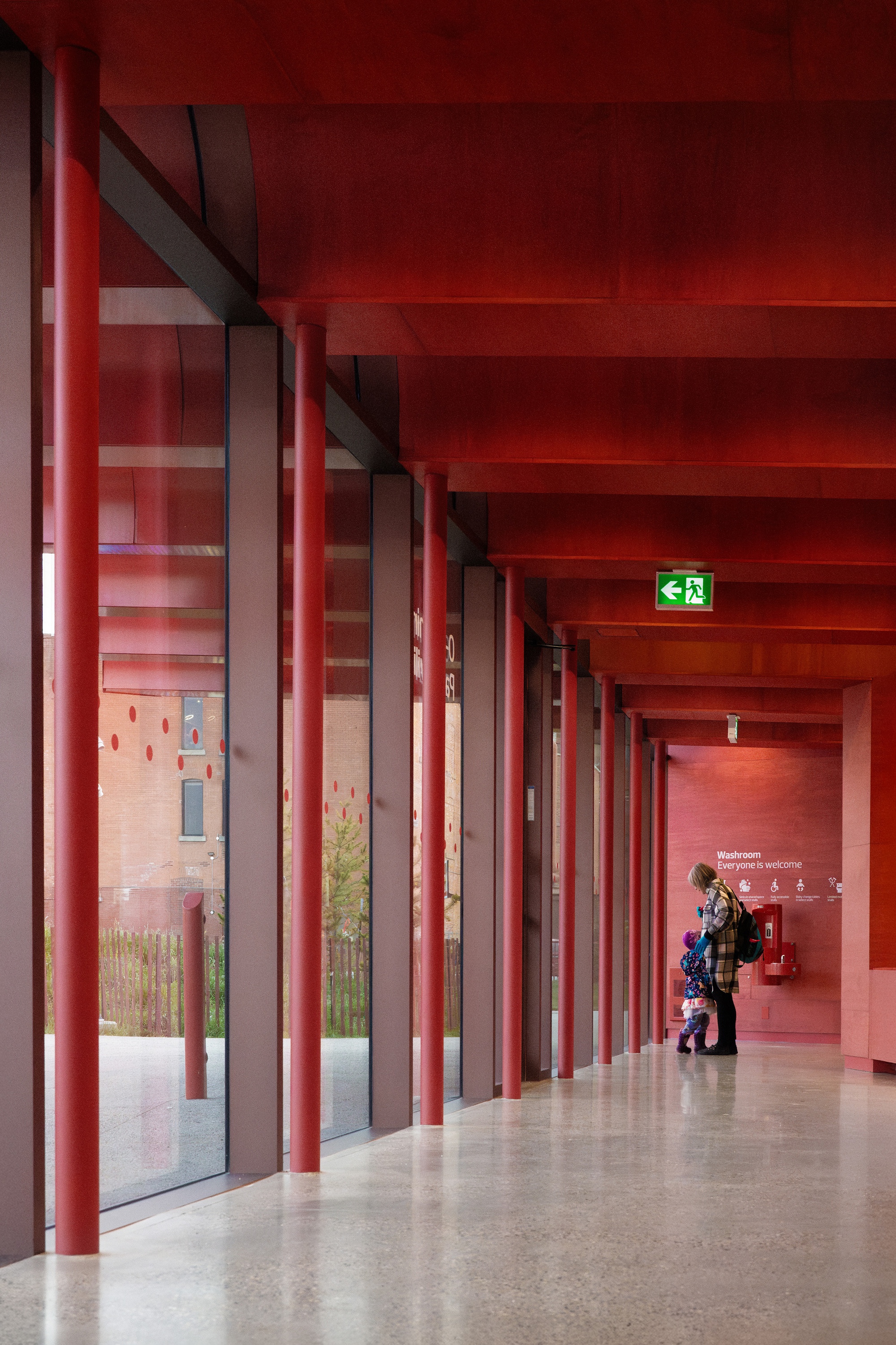 Interior corridor with red steel columns and red-painted ceiling beams with a figure walking