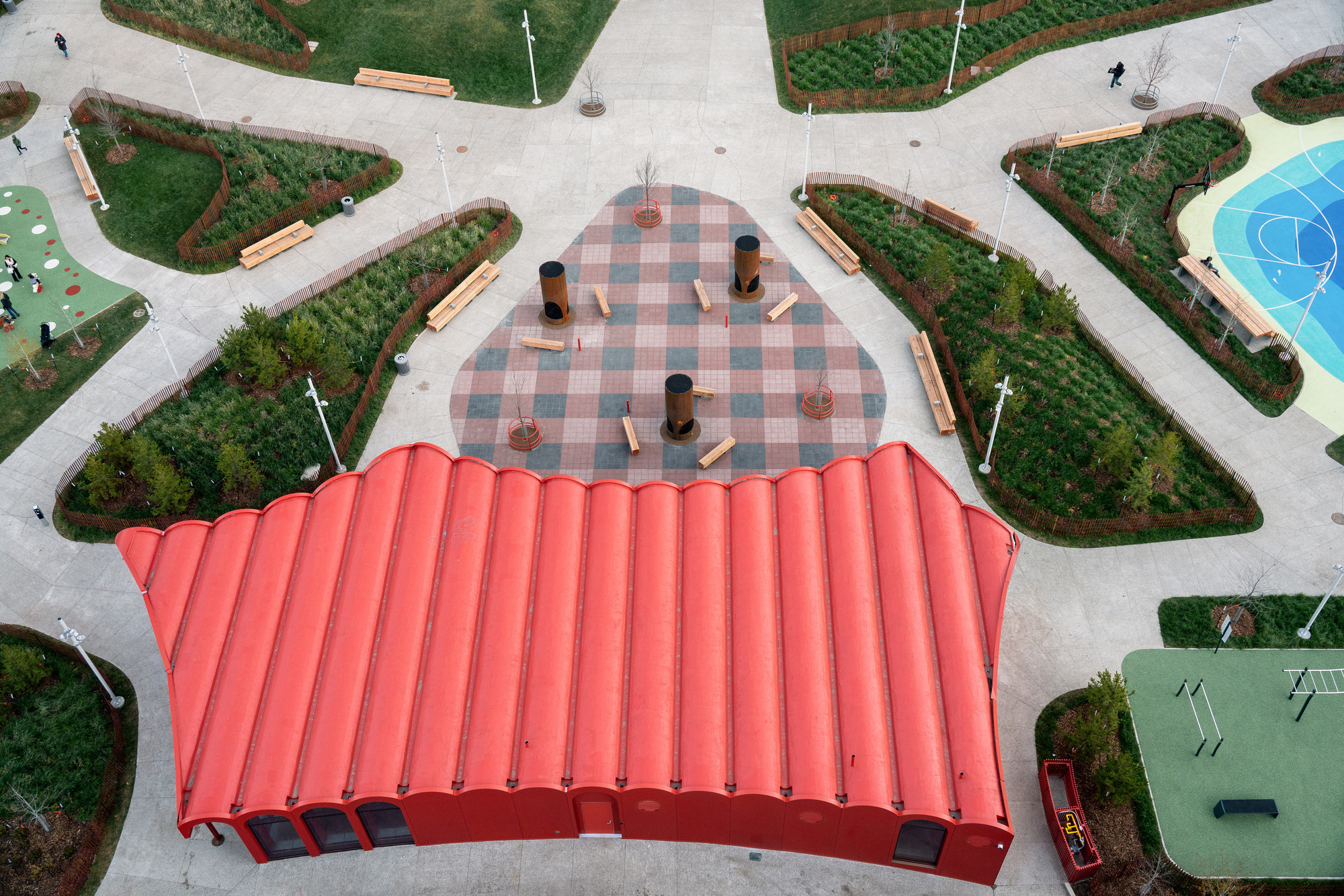 Aerial view of the undulating red roof sheltering a chequered plaza surrounded by planted garden beds