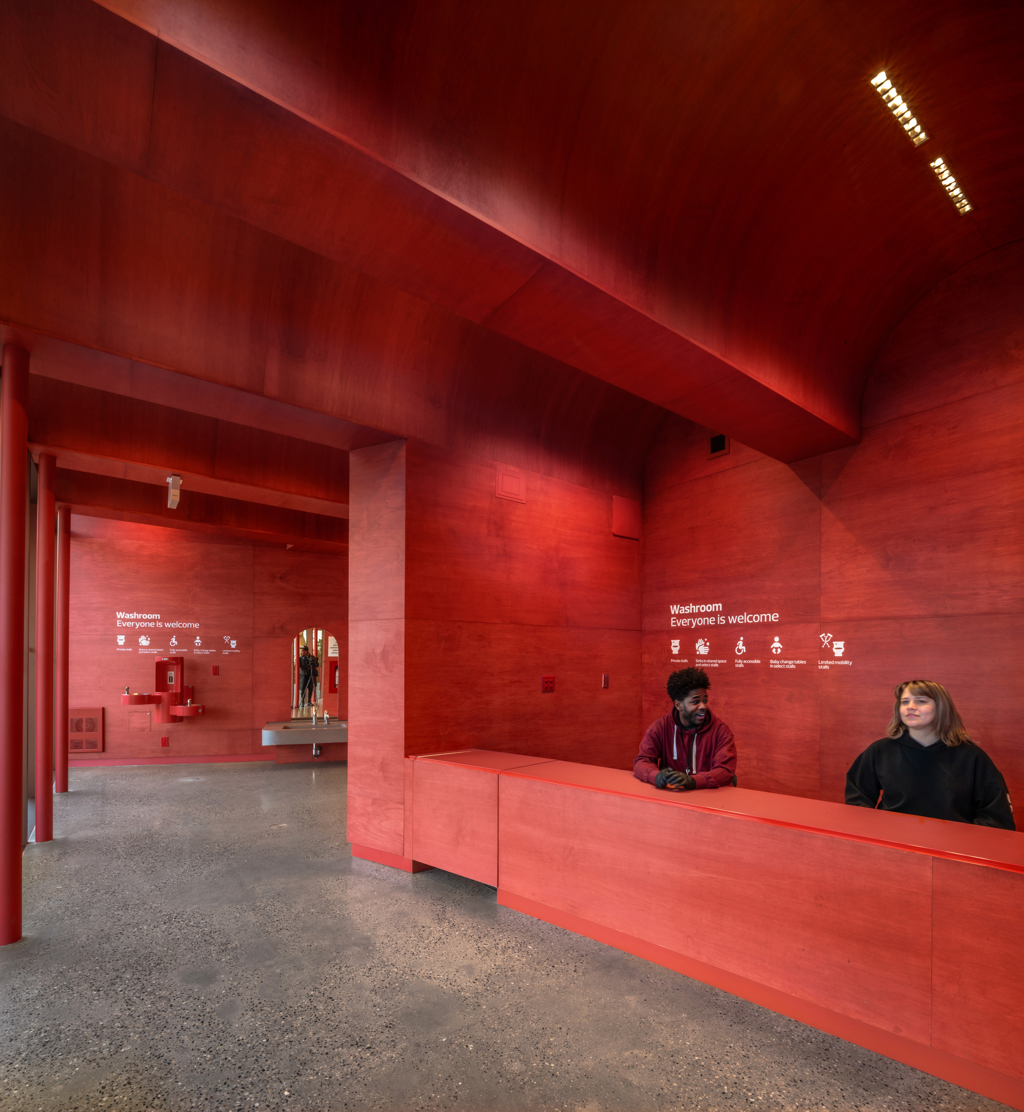 Red plywood entrance lobby with reception desk and two staff members beneath a vaulted ceiling