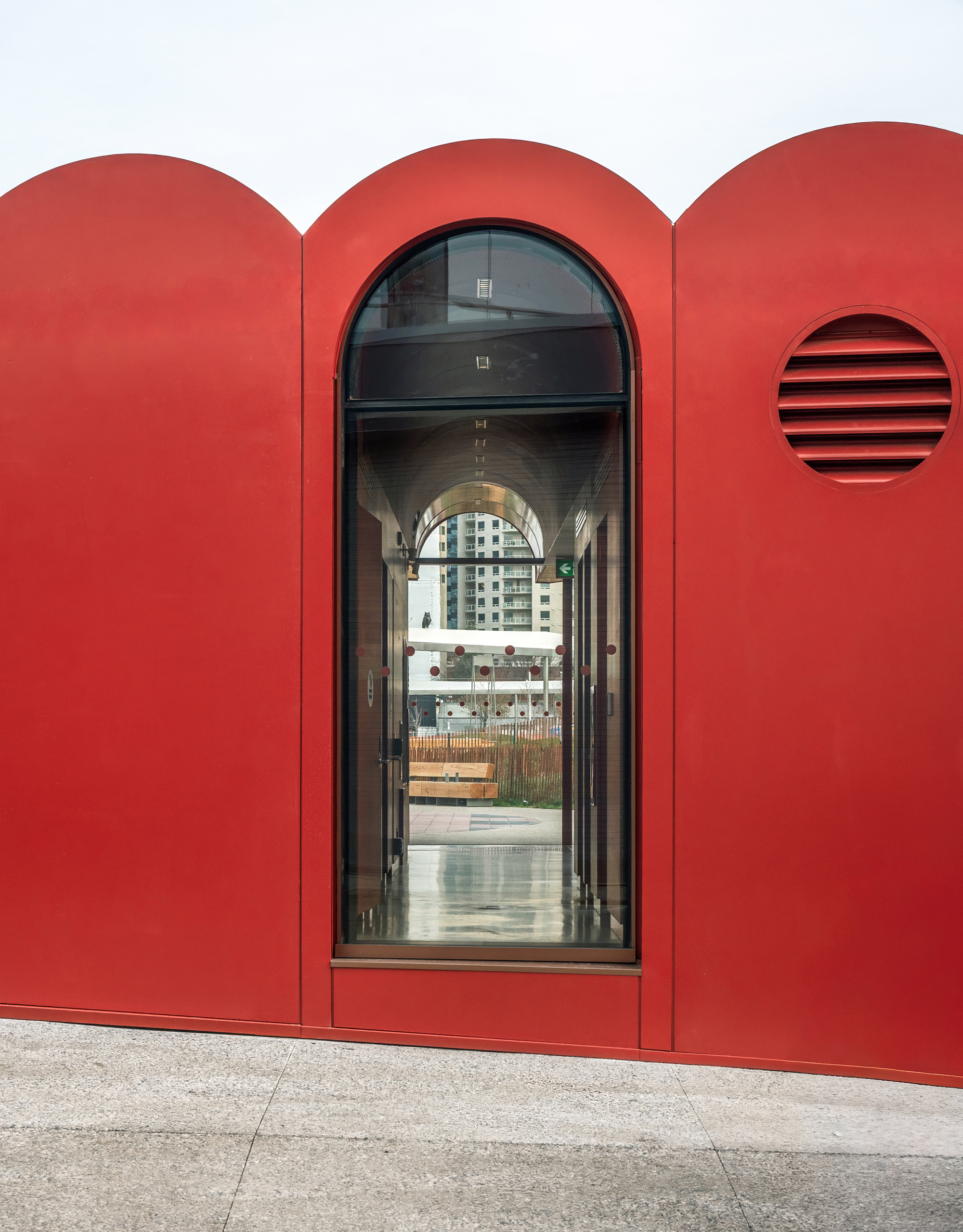 Arched doorway in red facade with circular vent opening and glazed entrance looking through to street