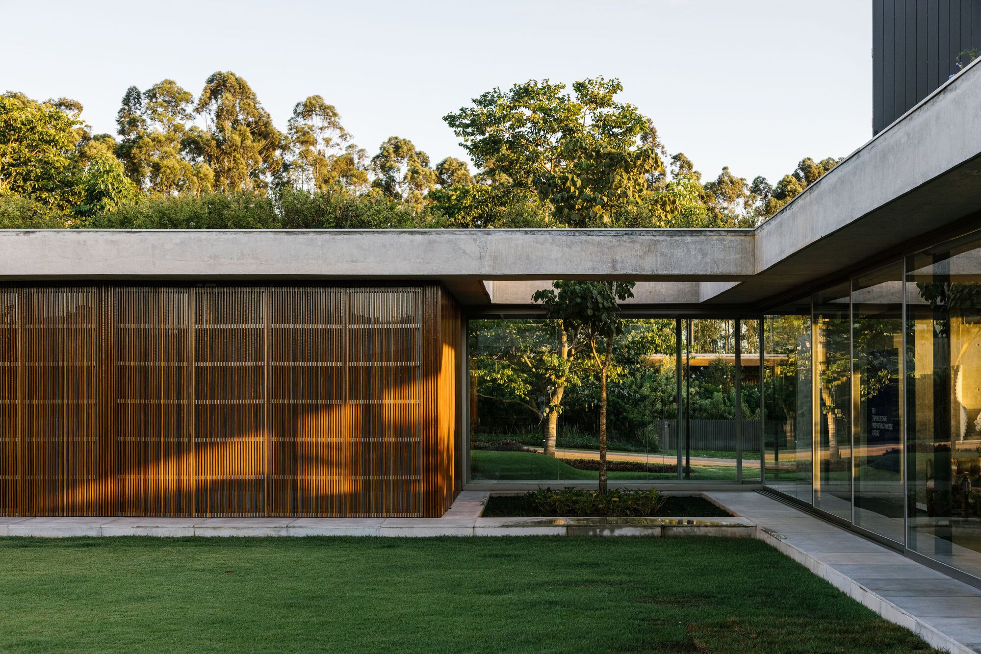 Slatted timber volume with concrete beam beside glass walls enclosing an interior courtyard garden