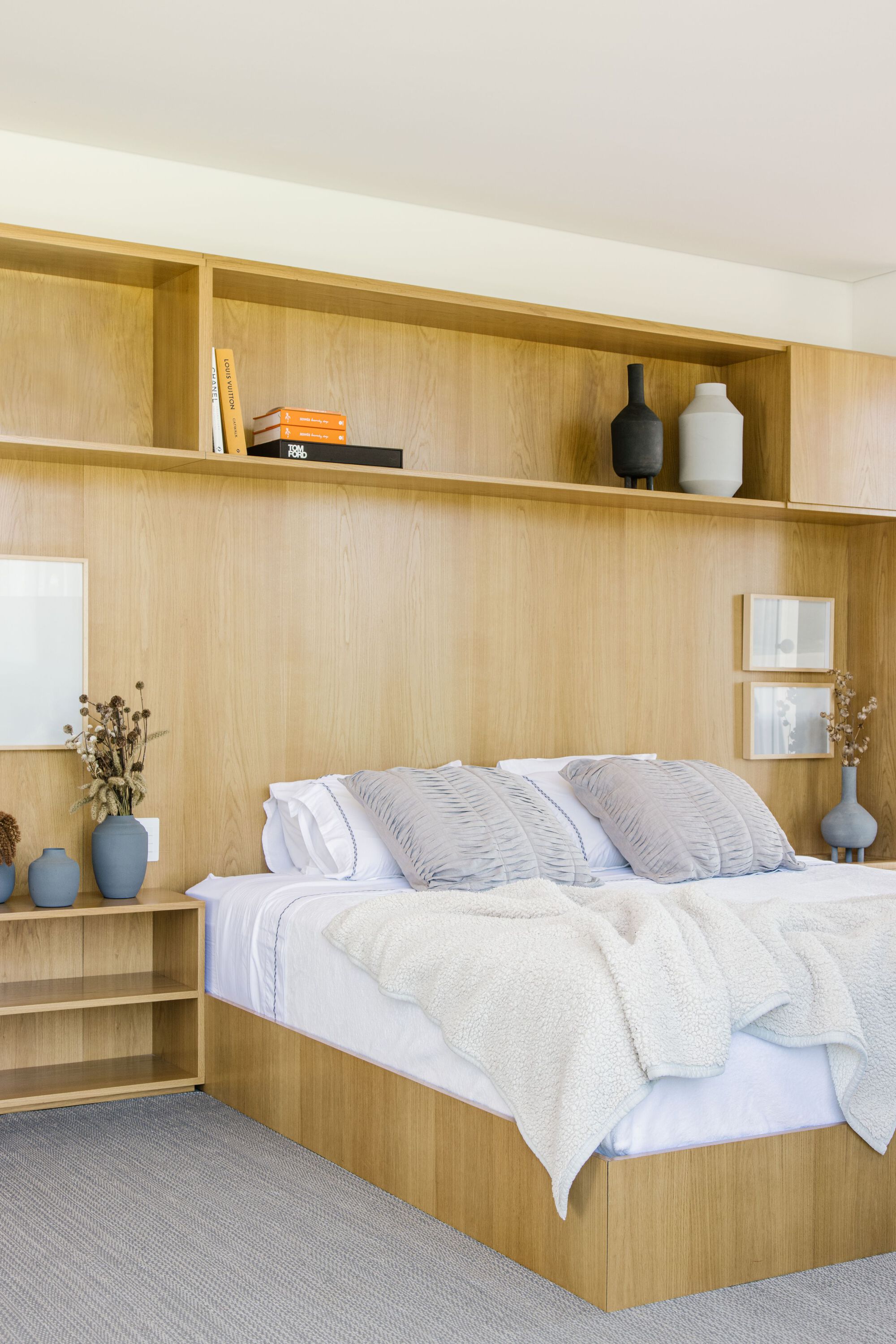 Built-in blonde wood bed platform with integrated shelving and overhead storage niches