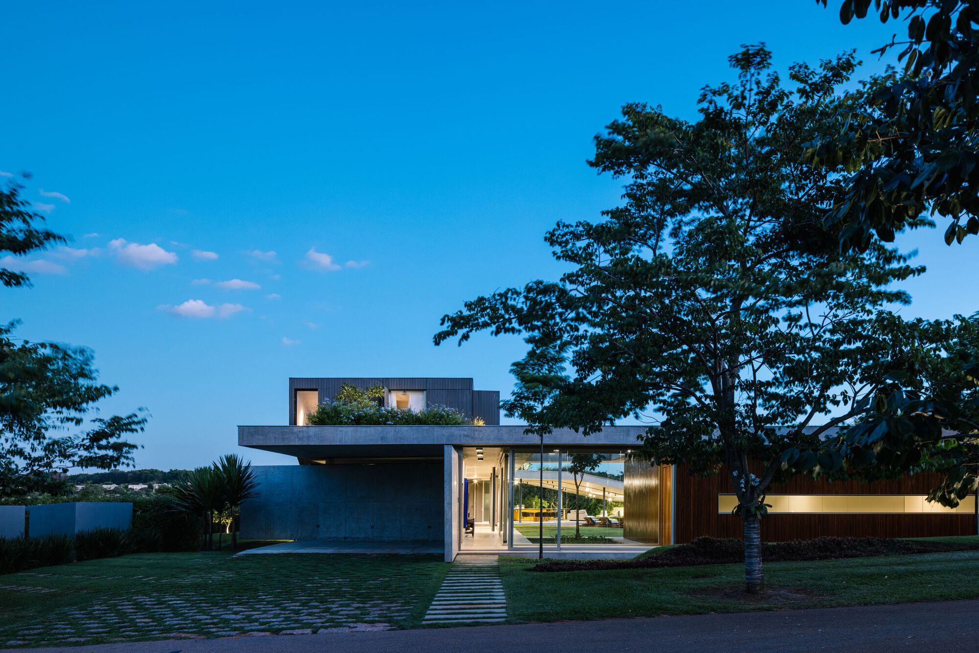 Street facade at dusk with illuminated interior visible through glazing and grid paver walkway