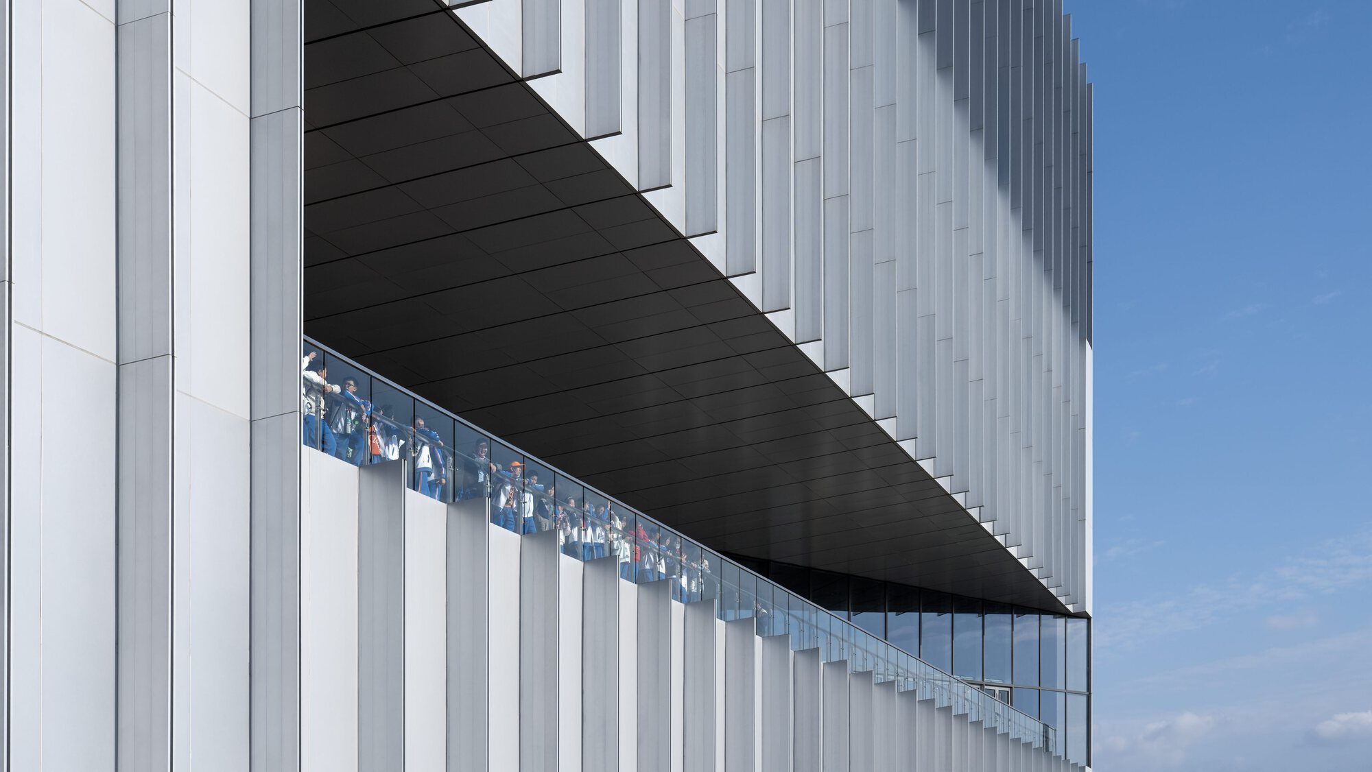 Exterior cantilever with vertical white metal fins and black soffit under blue sky
