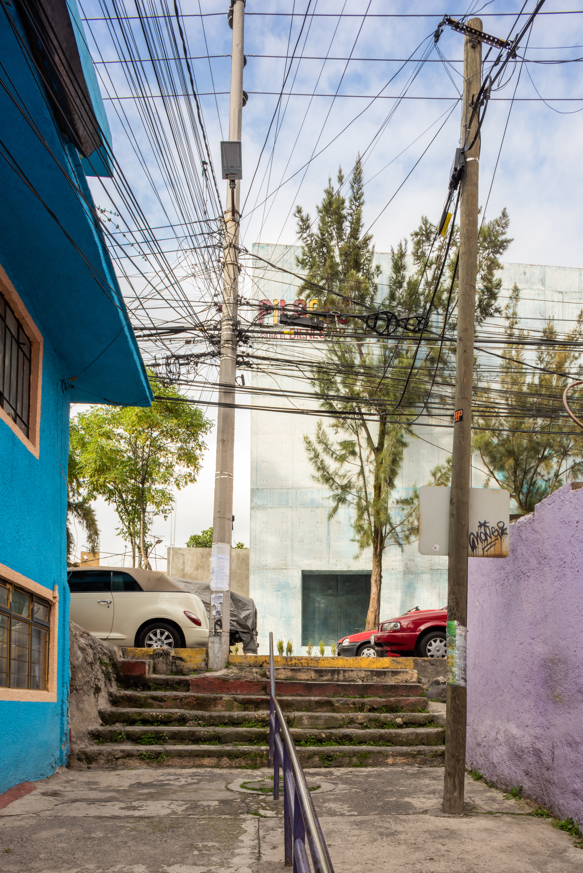 View up the street stair toward the concrete volume beneath overhead power lines and tall trees