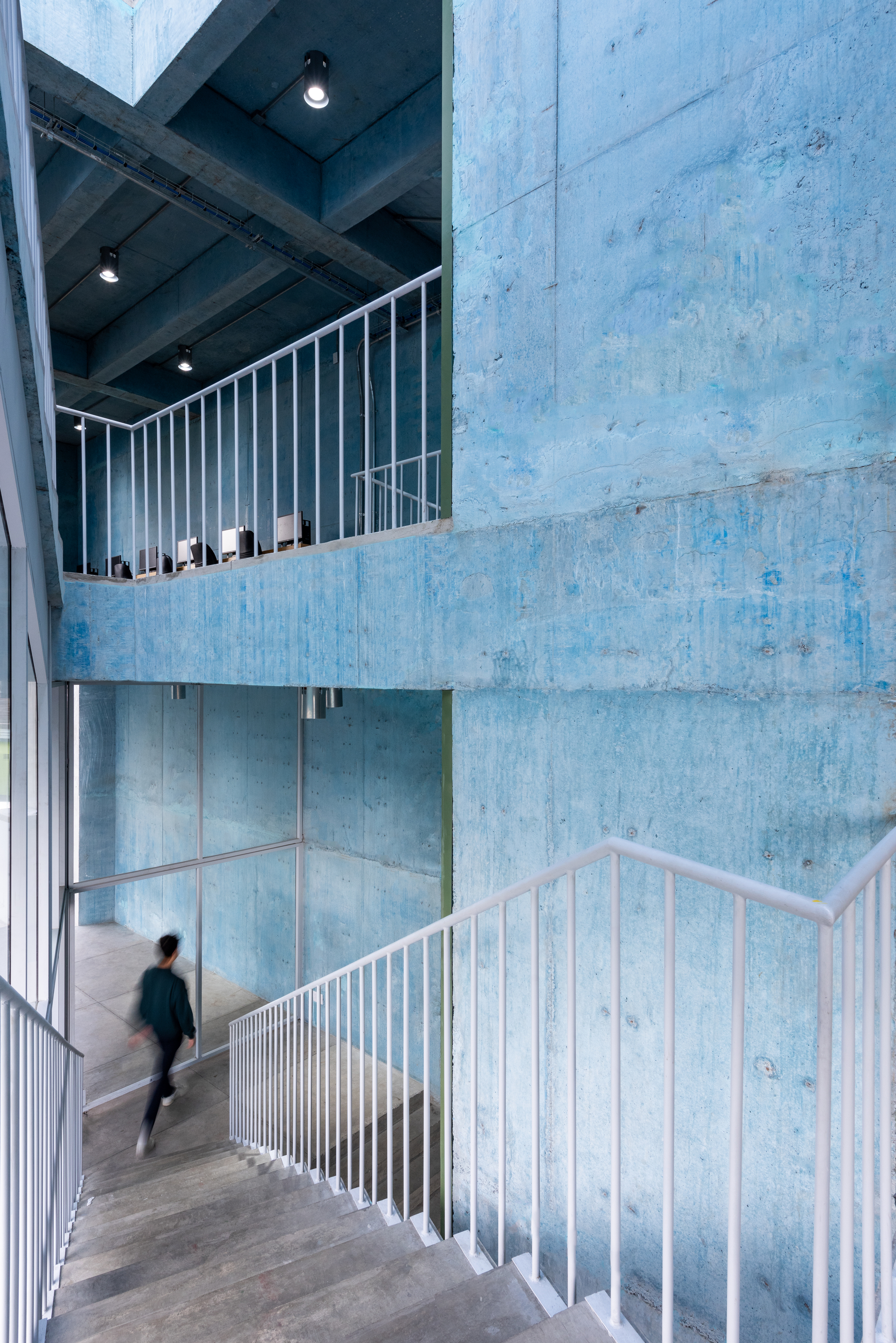 Interior stair with white railings connecting floors of tinted concrete walls as a person descends