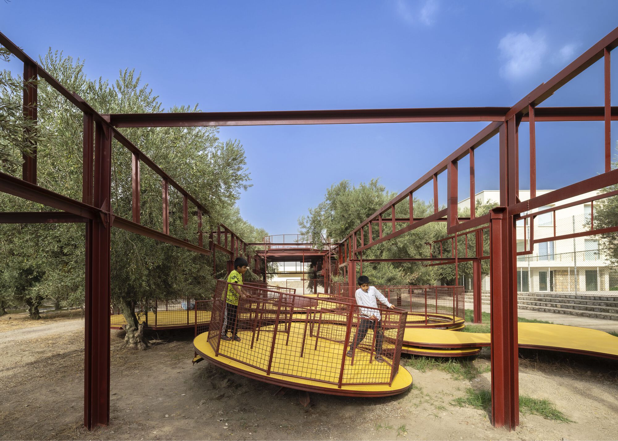 Red steel frame structure supporting yellow platforms beneath a blue sky with scattered clouds