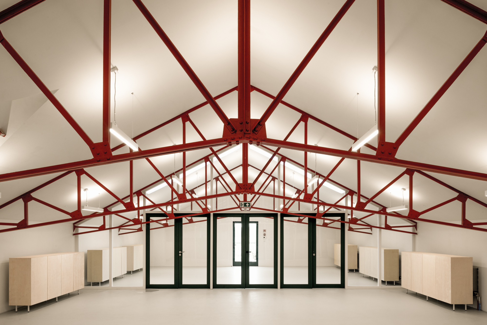 Interior hall with red steel truss system radiating from central ridge under vaulted white ceiling
