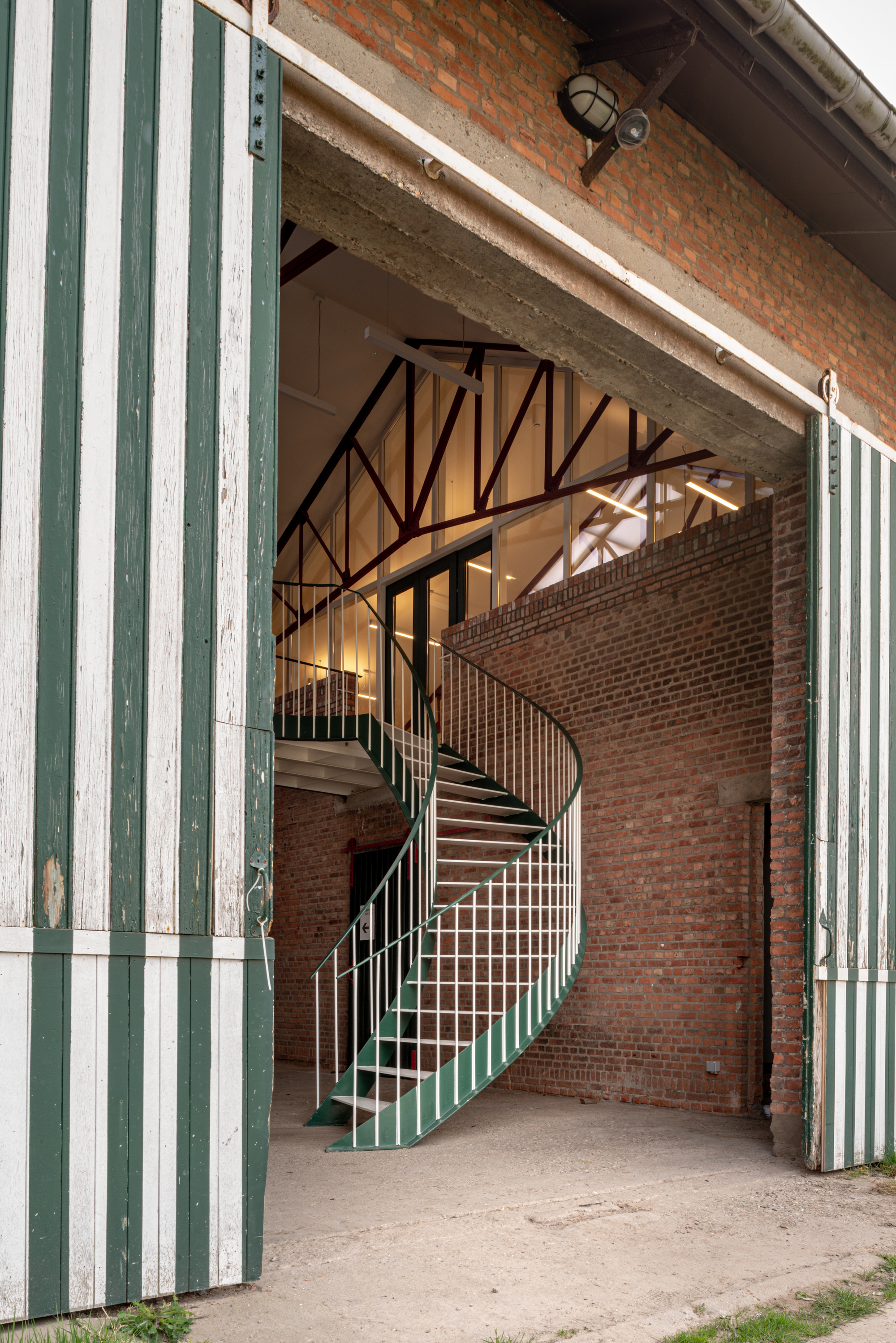 Green-and-white striped sliding barn doors framing a spiral staircase against an exposed brick wall