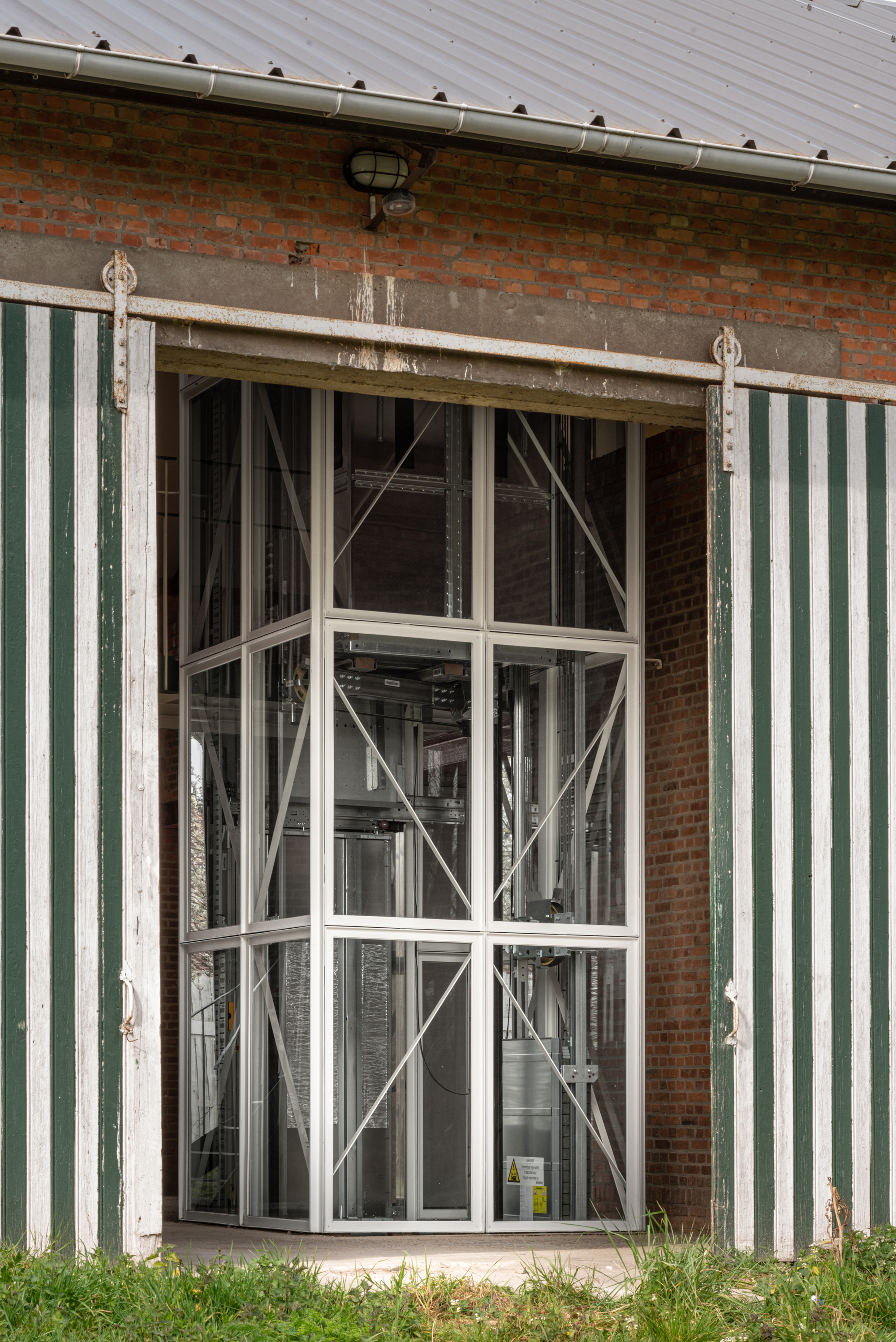 Exterior view of the glass elevator enclosure between green-and-white striped corrugated metal walls