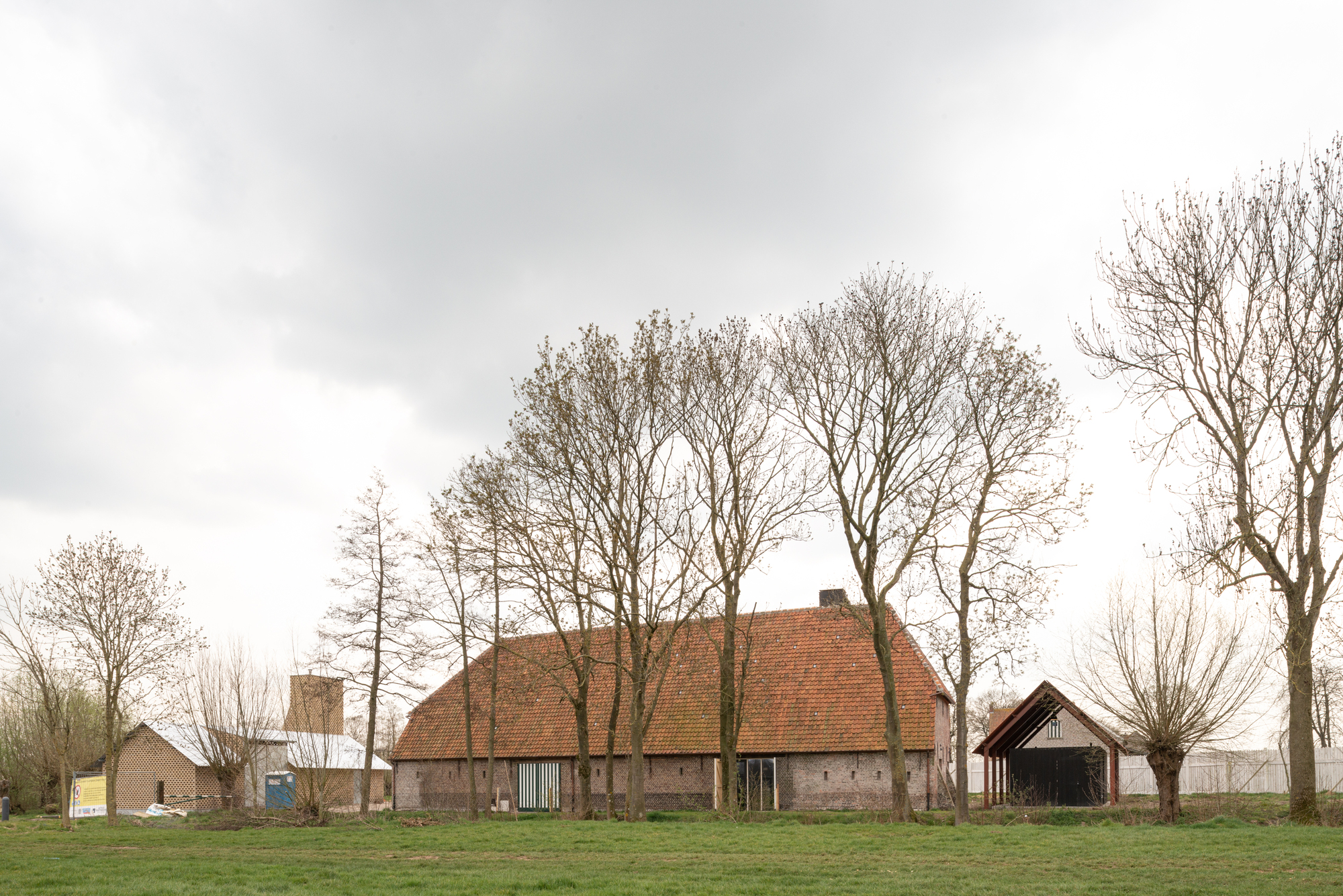 Farmhouse complex with clay tile roofs surrounded by bare winter trees in a grassy field