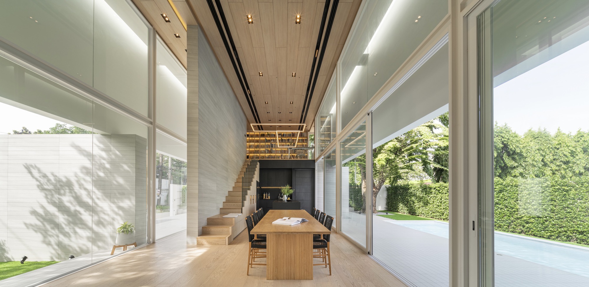 Double-height dining space with timber staircase and slatted ceiling under indirect lighting