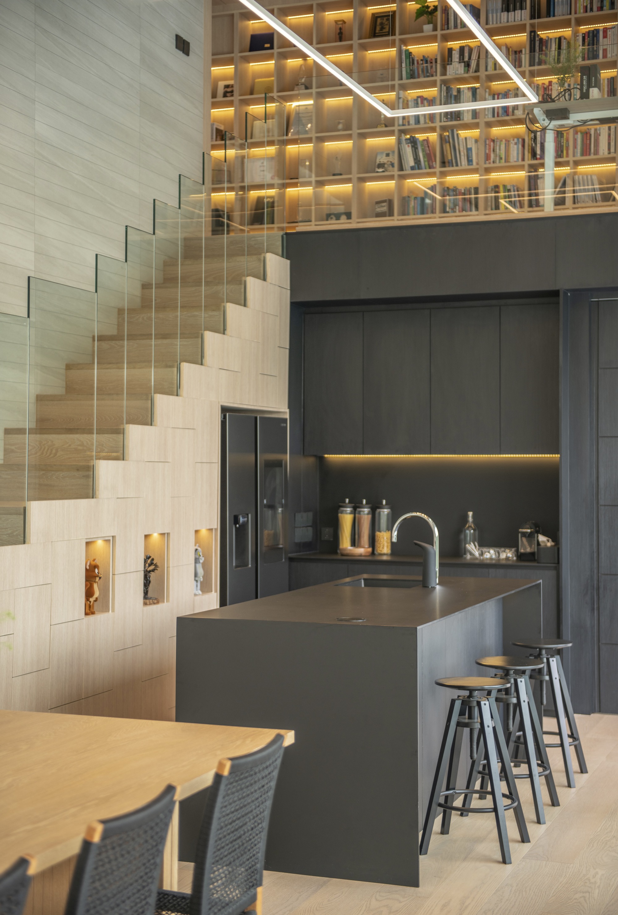 Kitchen island with bar seating below timber stairs and backlit library shelving