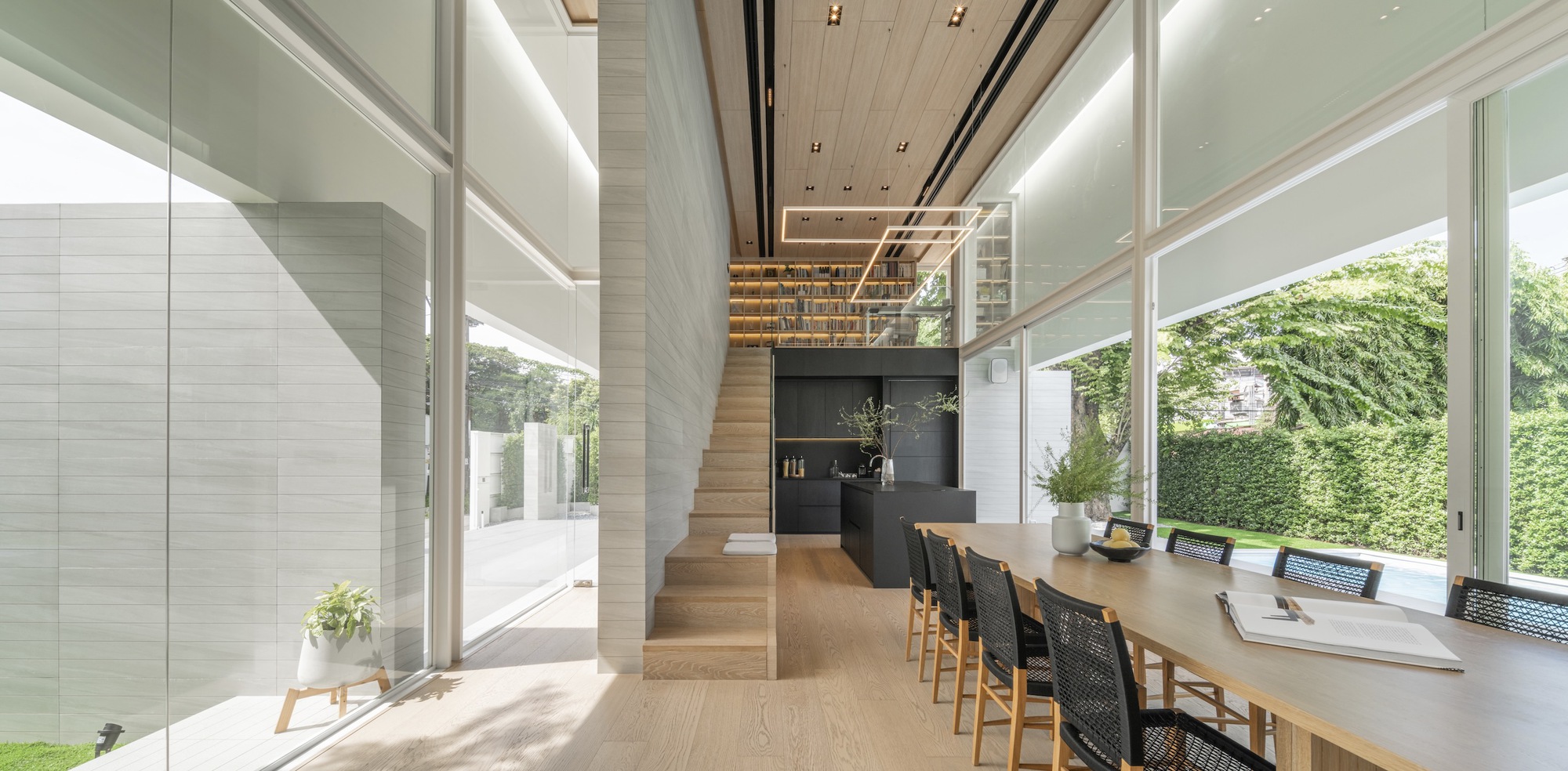 Living and dining space with floor-to-ceiling glazing opening onto lawn and hedge beyond