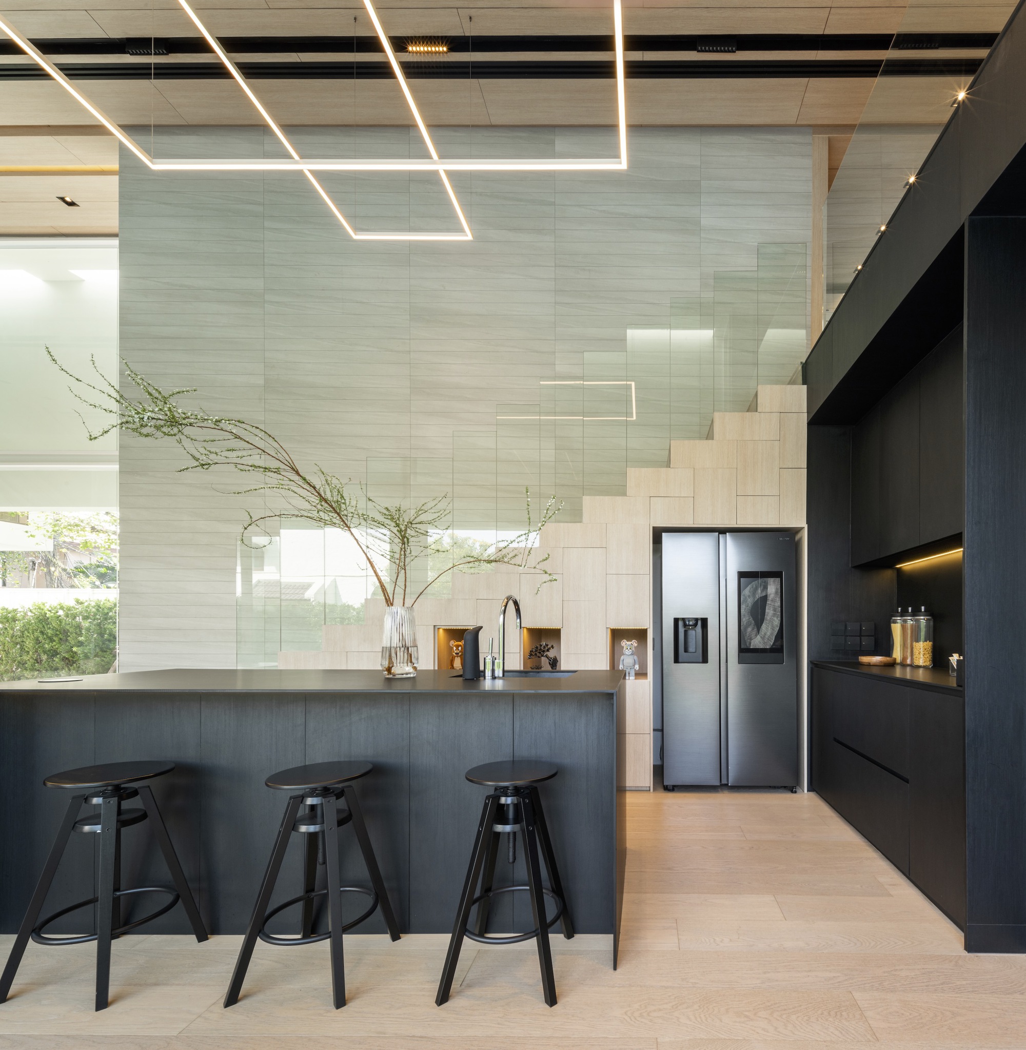 Black kitchen counter with bar stools beneath geometric linear light fixtures and tile wall