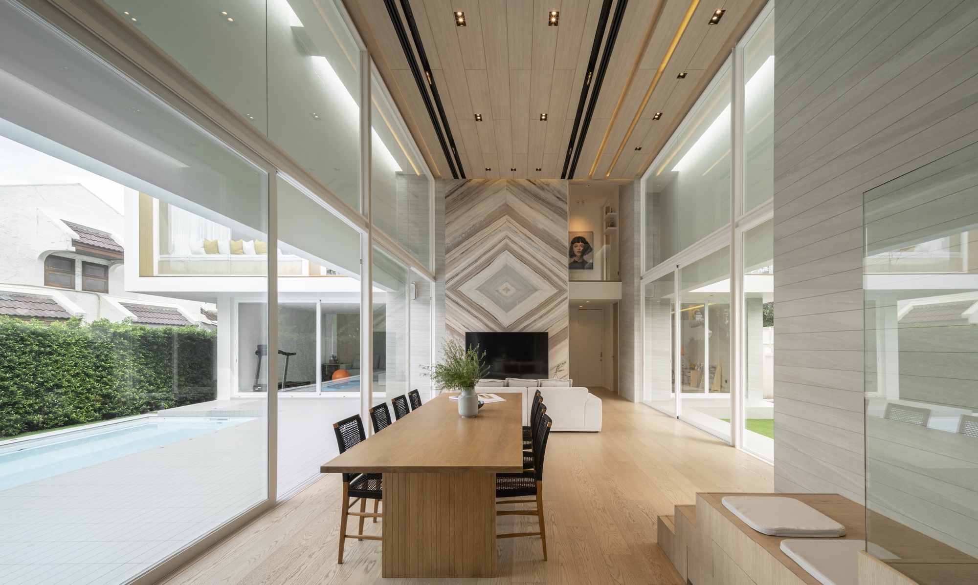 Double-height dining space with timber ceiling, chevron-patterned fireplace wall and floor-to-ceiling glass overlooking the lawn