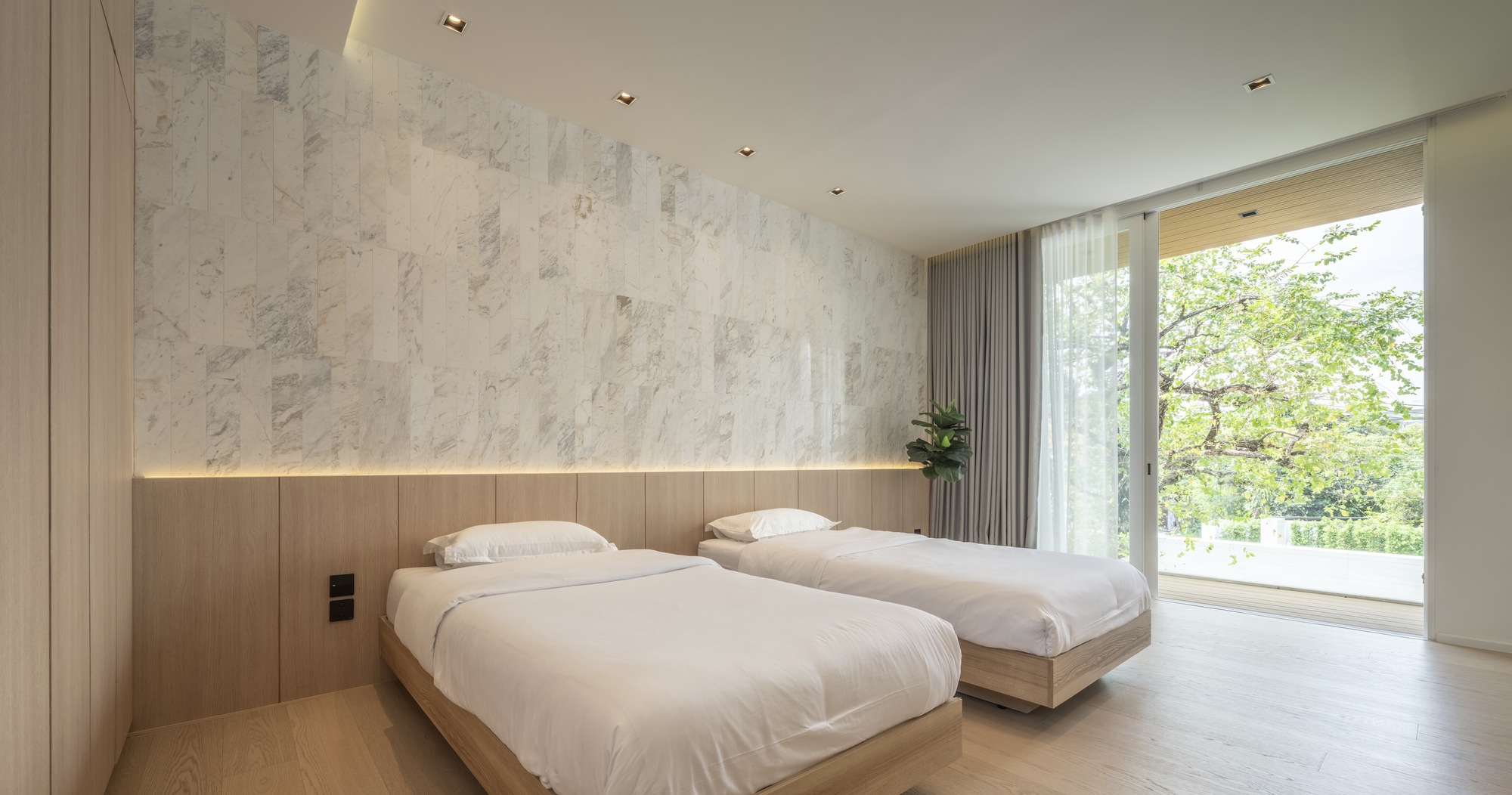 Bedroom with two timber-clad beds beneath a pale marble accent wall and garden views