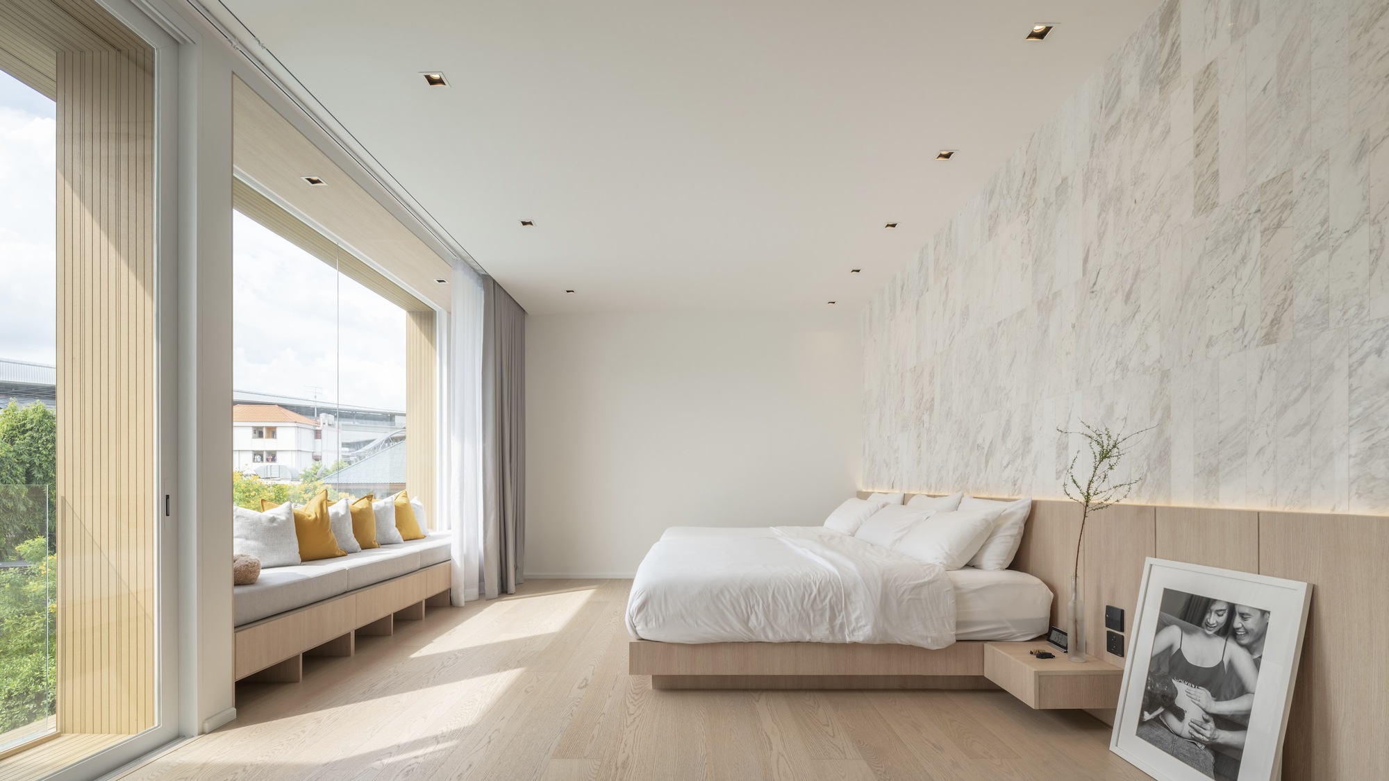 Bedroom with window seat, timber bed and marble wall panel illuminated by morning sunlight