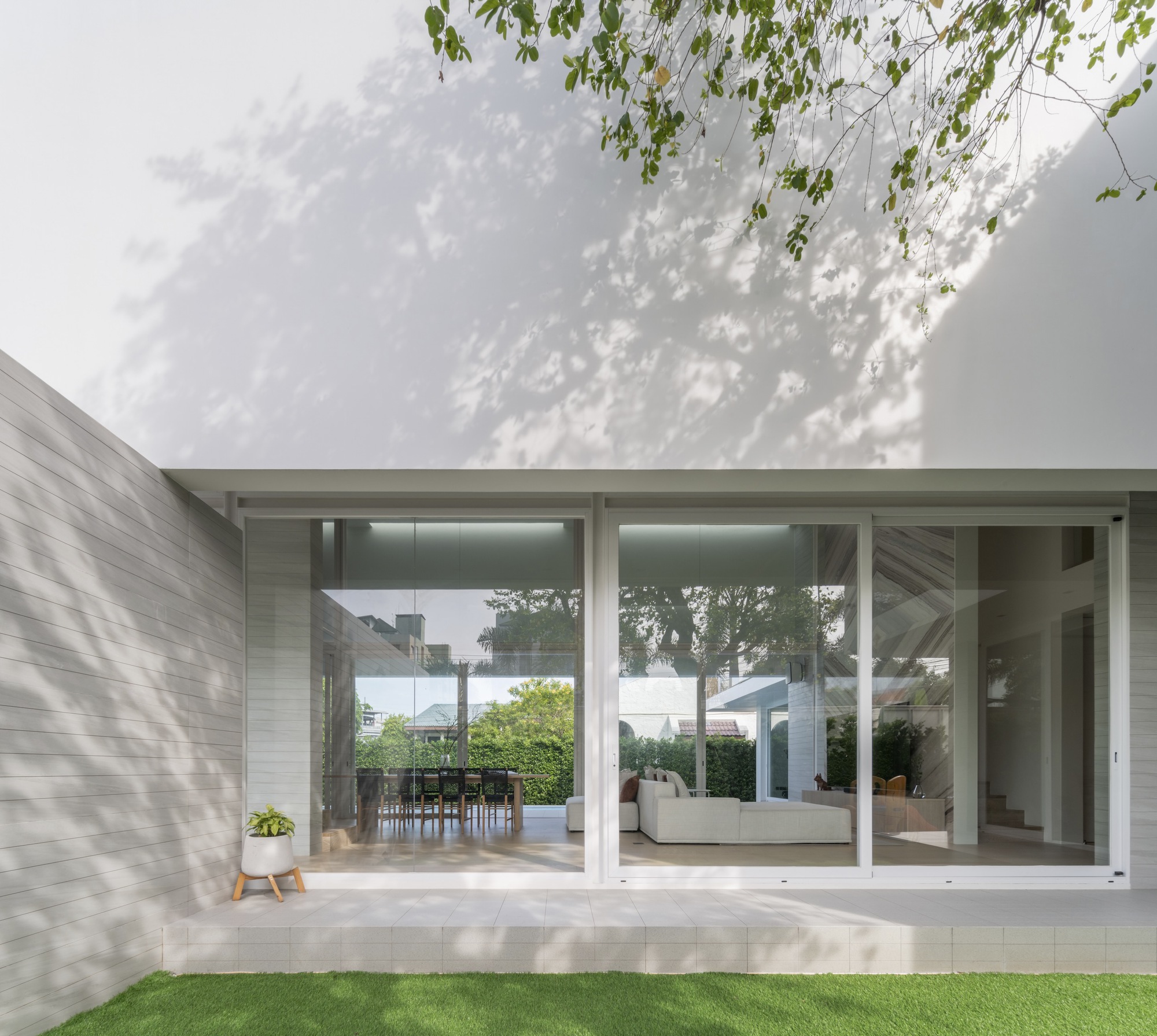 Glass corner facade with dappled tree shadows on white walls and lawn in foreground