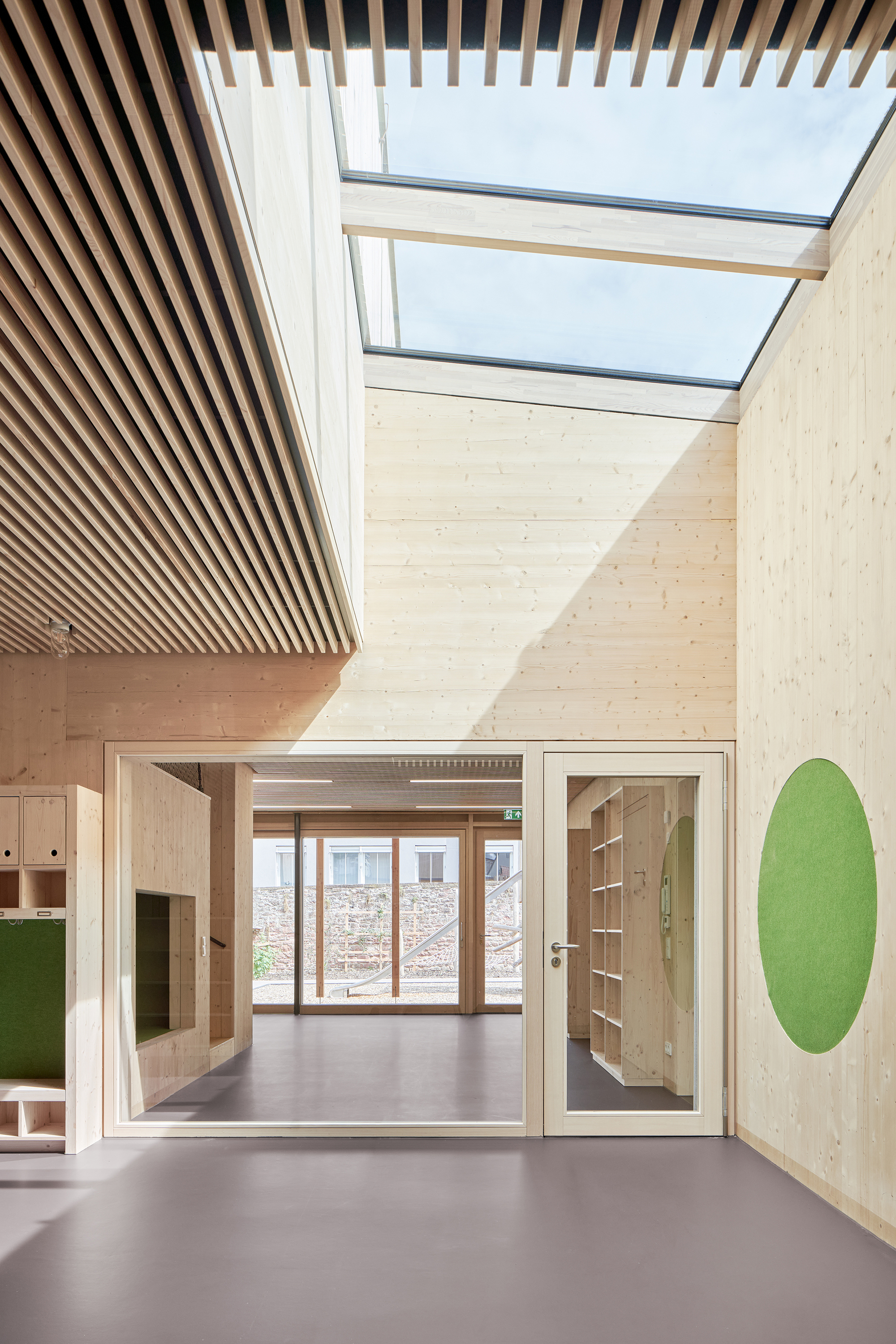 Interior hallway with timber slatted ceiling, skylights, and green circular wall graphic near doorways