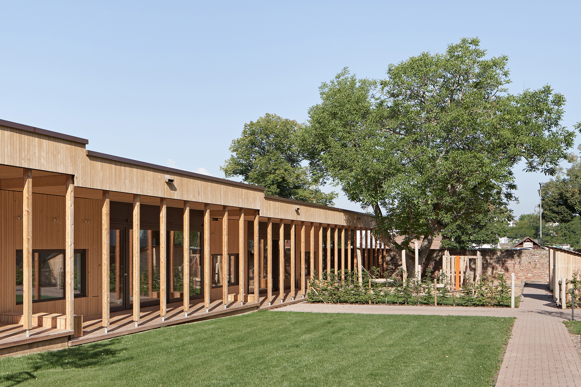 Long elevation showing repeated timber columns along glazed facade with lawn and mature tree canopy
