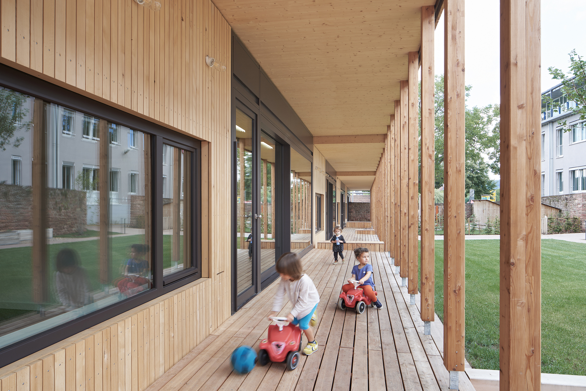Covered timber walkway with exposed columns and decking where children play with toy cars