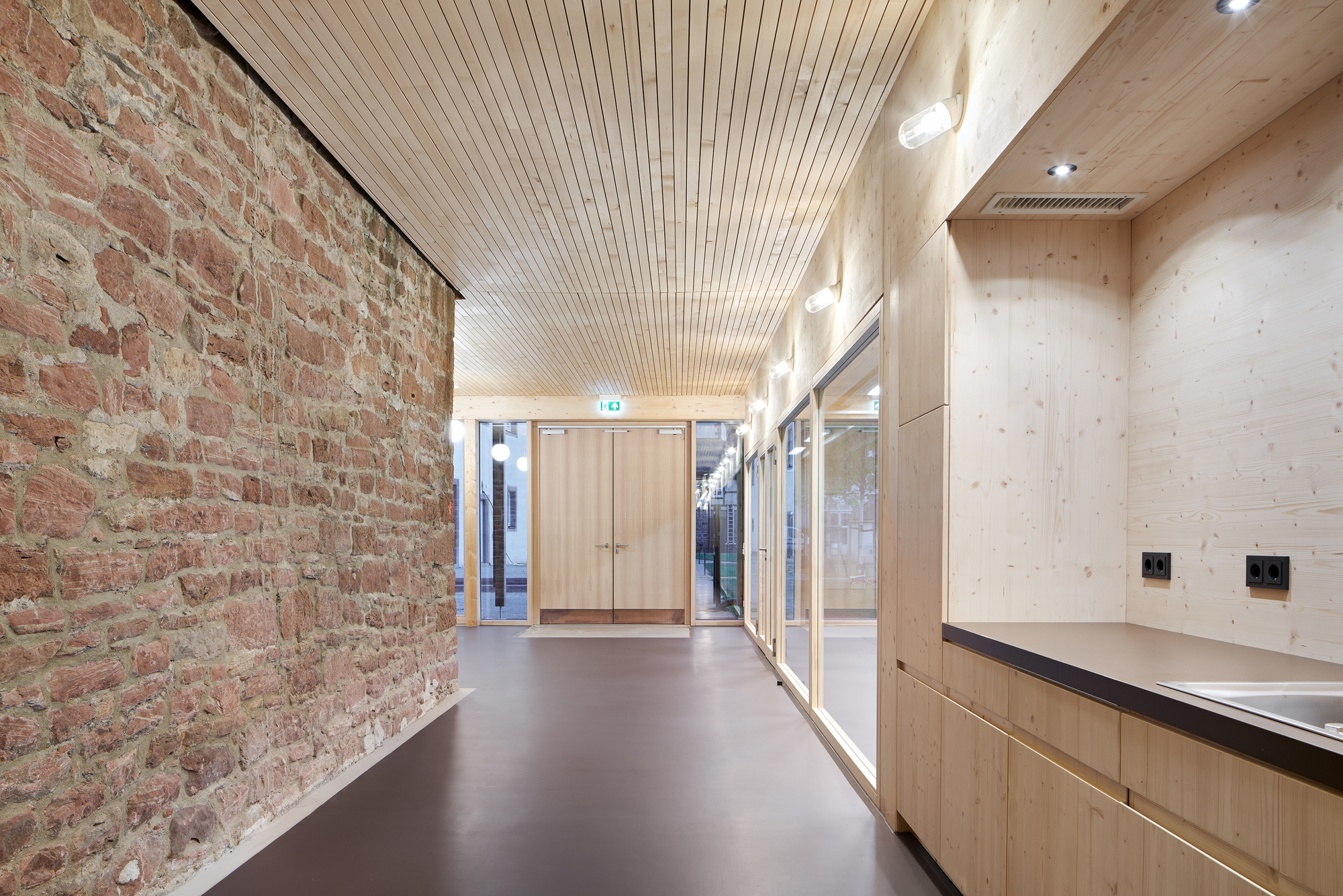 Hallway with exposed brick wall, timber cabinetry and slatted ceiling under daylight