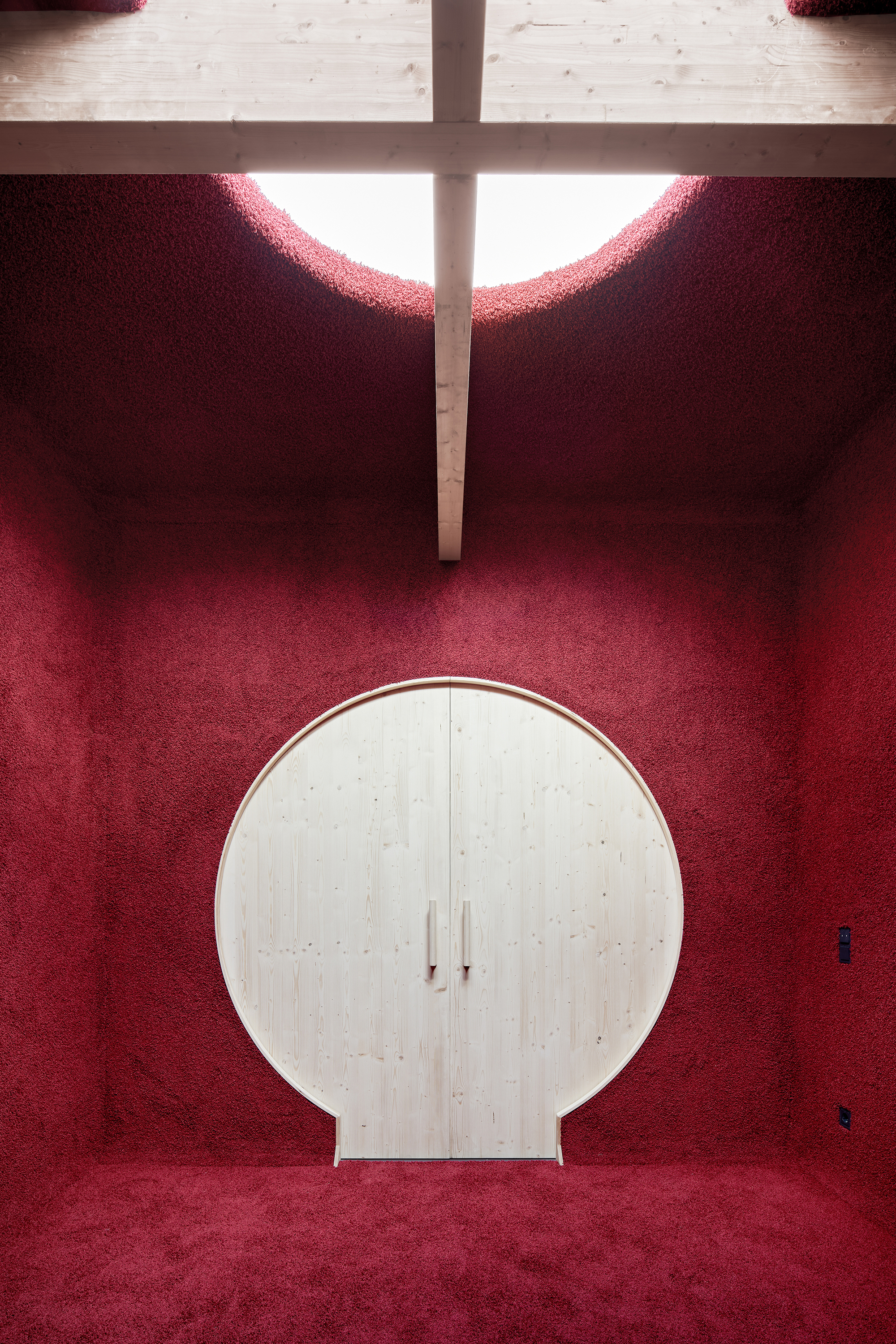 Circular plywood cabinet against deep red carpeted walls beneath a clerestory cross