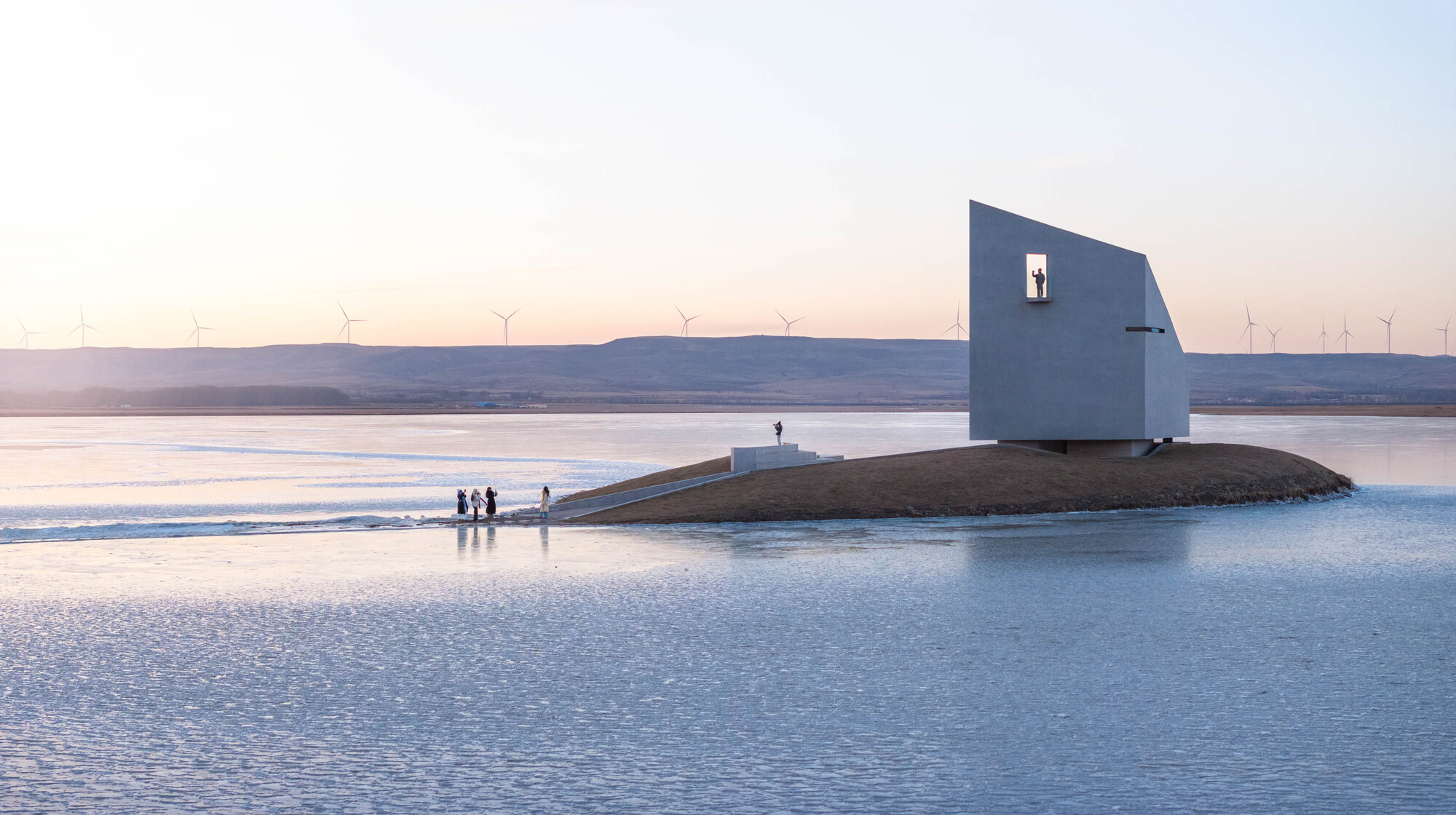 White cubic volume with square window on artificial mound surrounded by ice and visitors at dusk