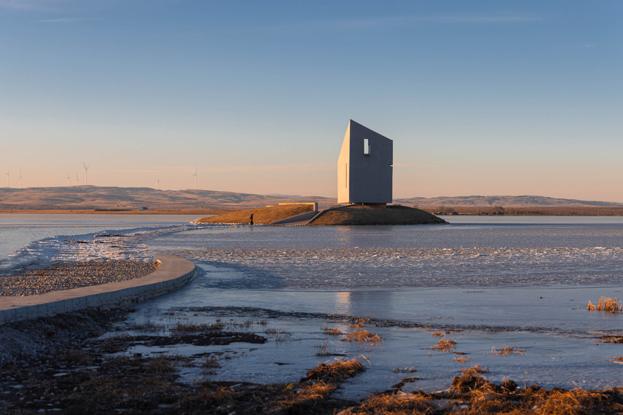 The angled facade with a single vertical window on the rocky outcrop at dusk