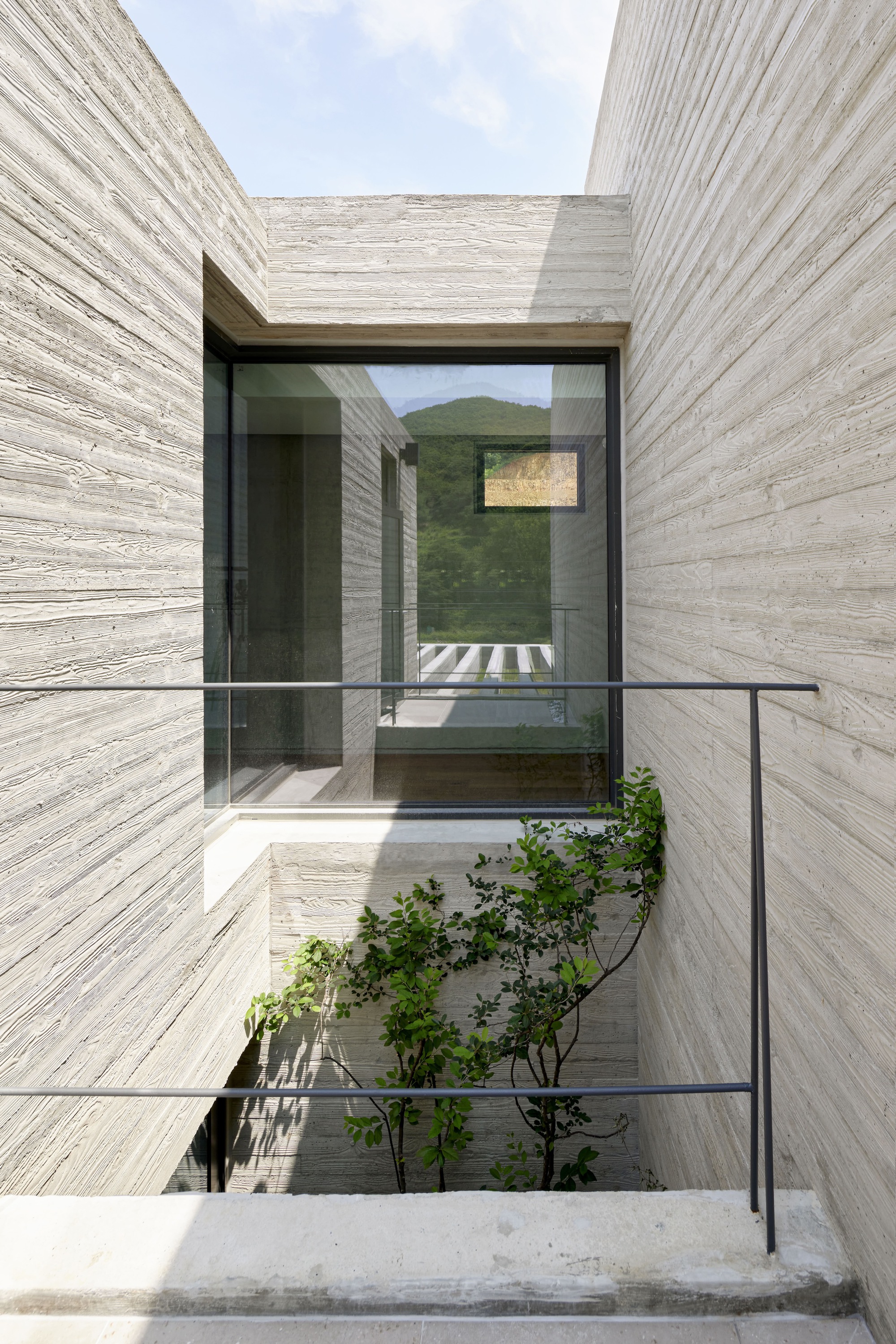 Concrete entry courtyard with glass bridge and planted tree beneath the mountain view