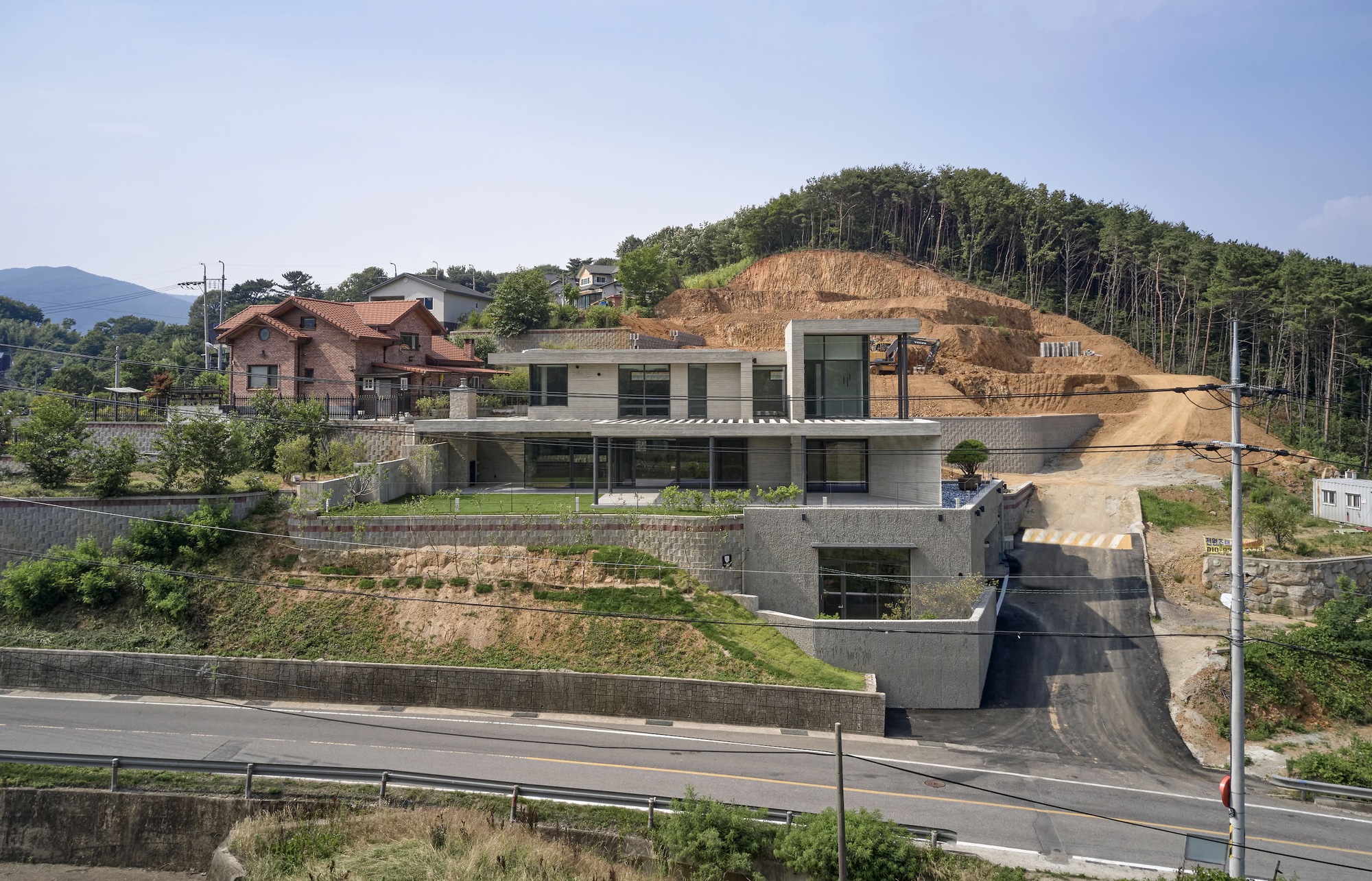 Hillside site showing the three-level house carved into the slope beside the highway