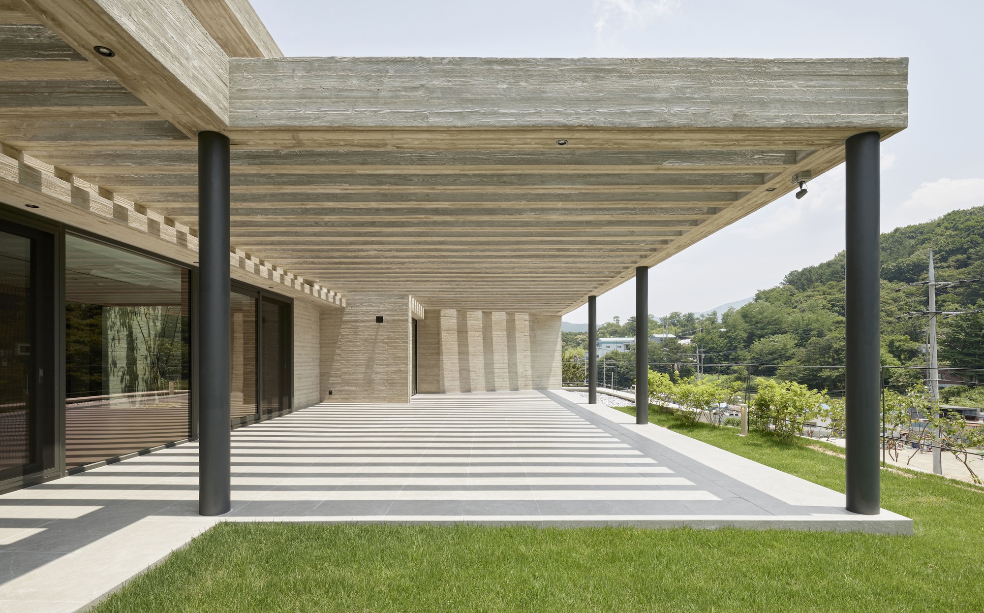 Covered terrace with exposed timber slat ceiling supported by black steel columns overlooking grass lawn