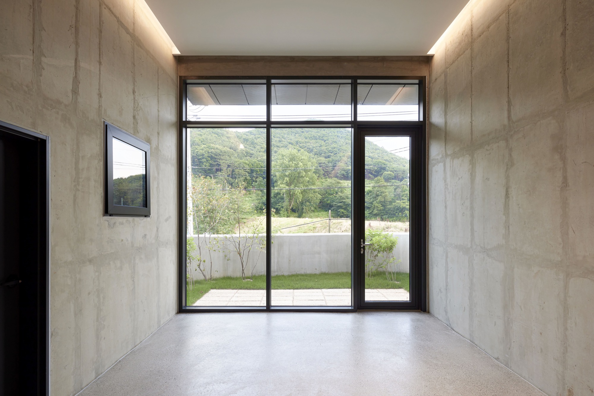 Entry vestibule with board-formed concrete walls and full-height glazed door framing hillside view beyond courtyard