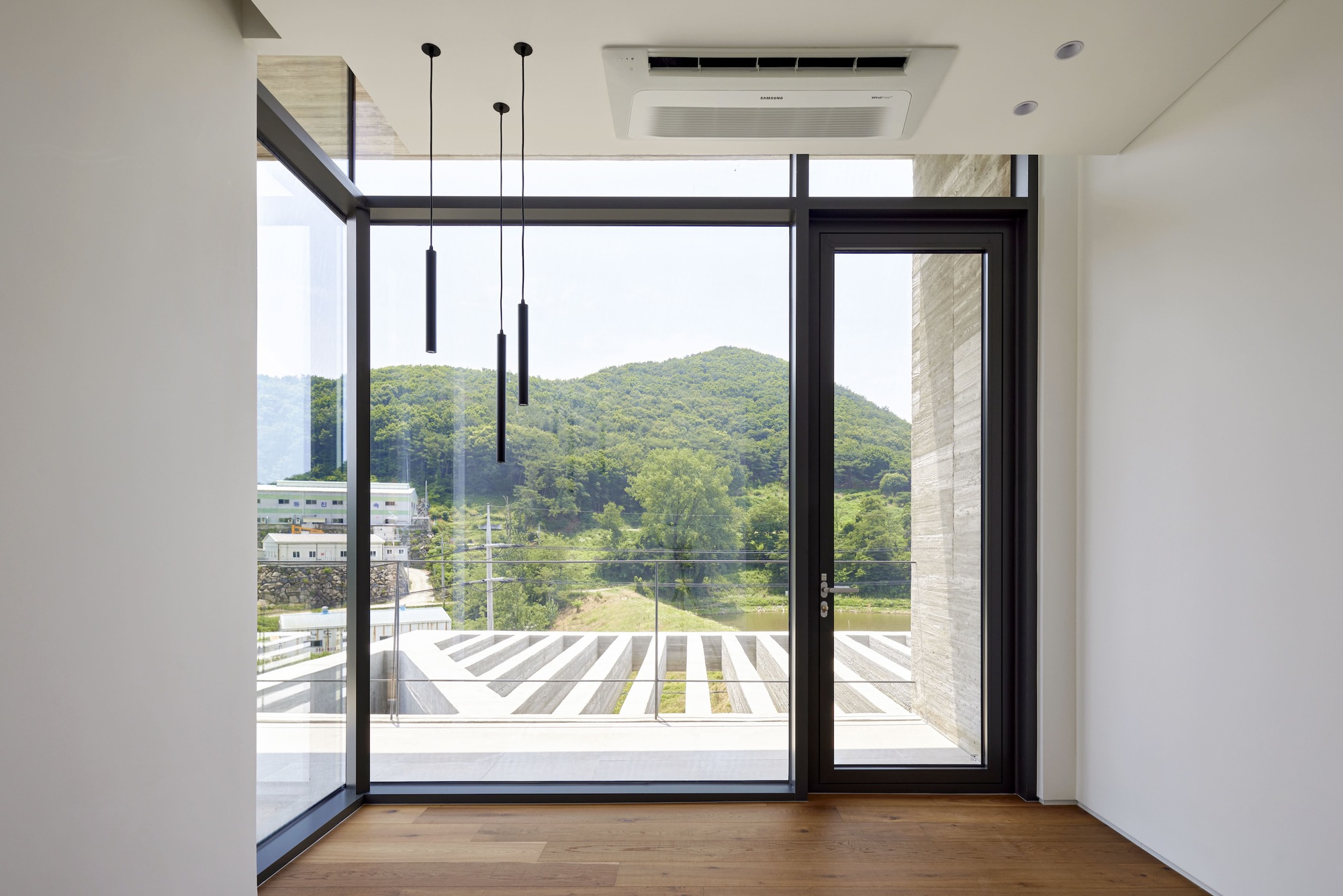 Interior room with timber floor and black-framed glazing overlooking a slatted deck and forested hillside