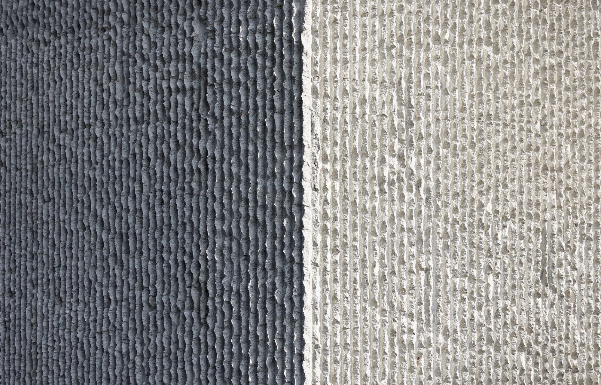 Close-up of two textured concrete panels showing dark grey and light grey ribbed formwork patterns