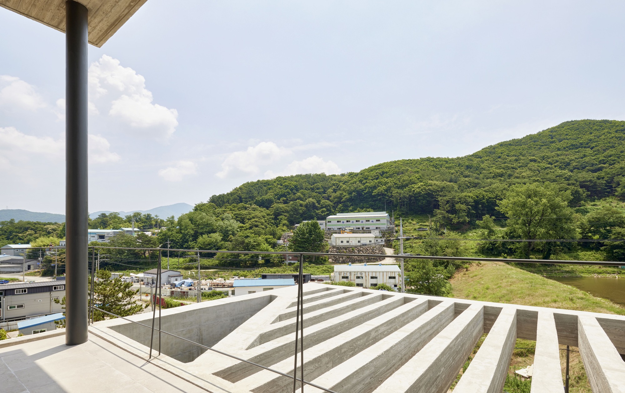 Rooftop terrace with glass balustrade overlooking striped concrete seating steps and forested hillside