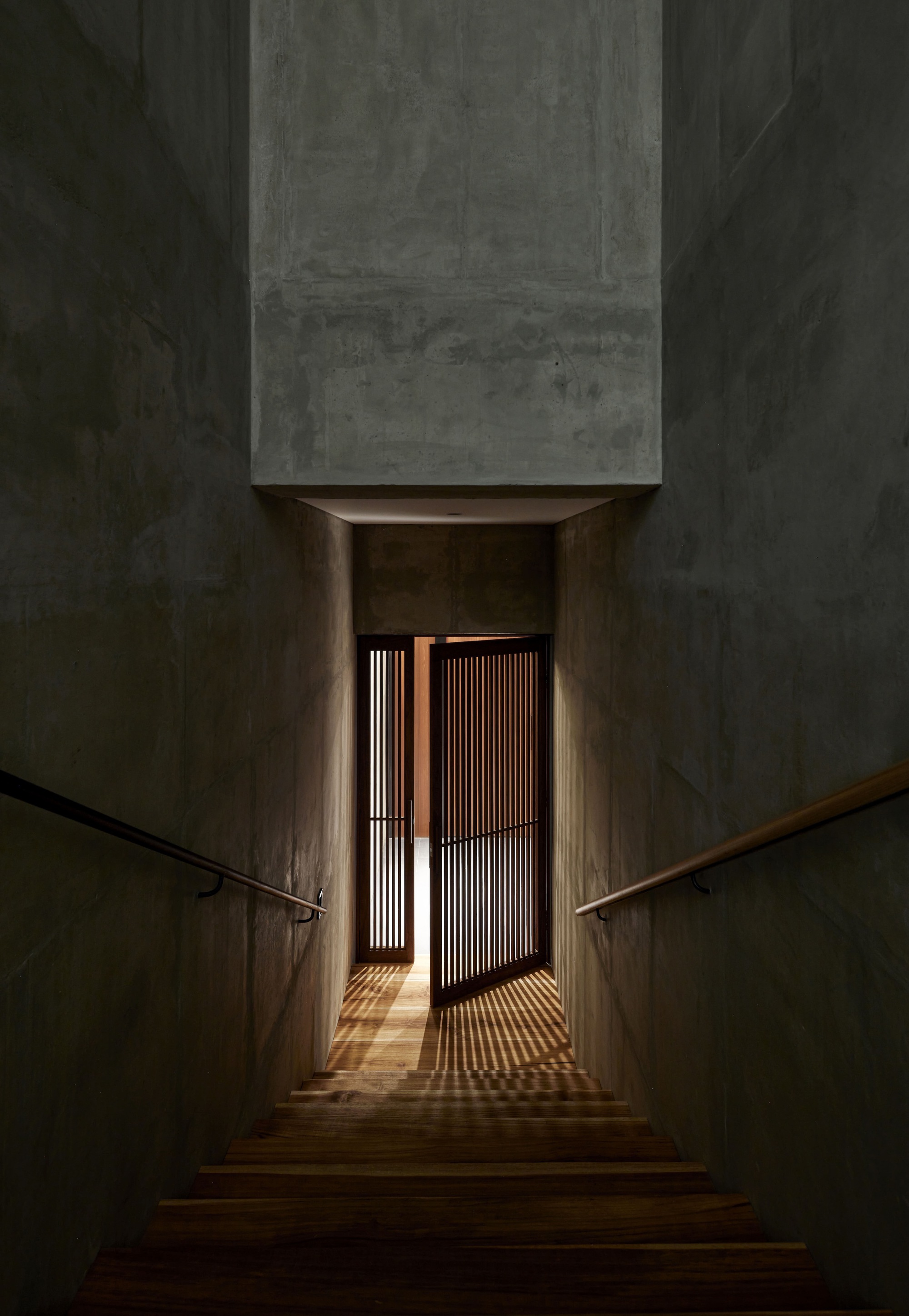 Interior staircase descending toward timber slat door with light filtering through at dusk